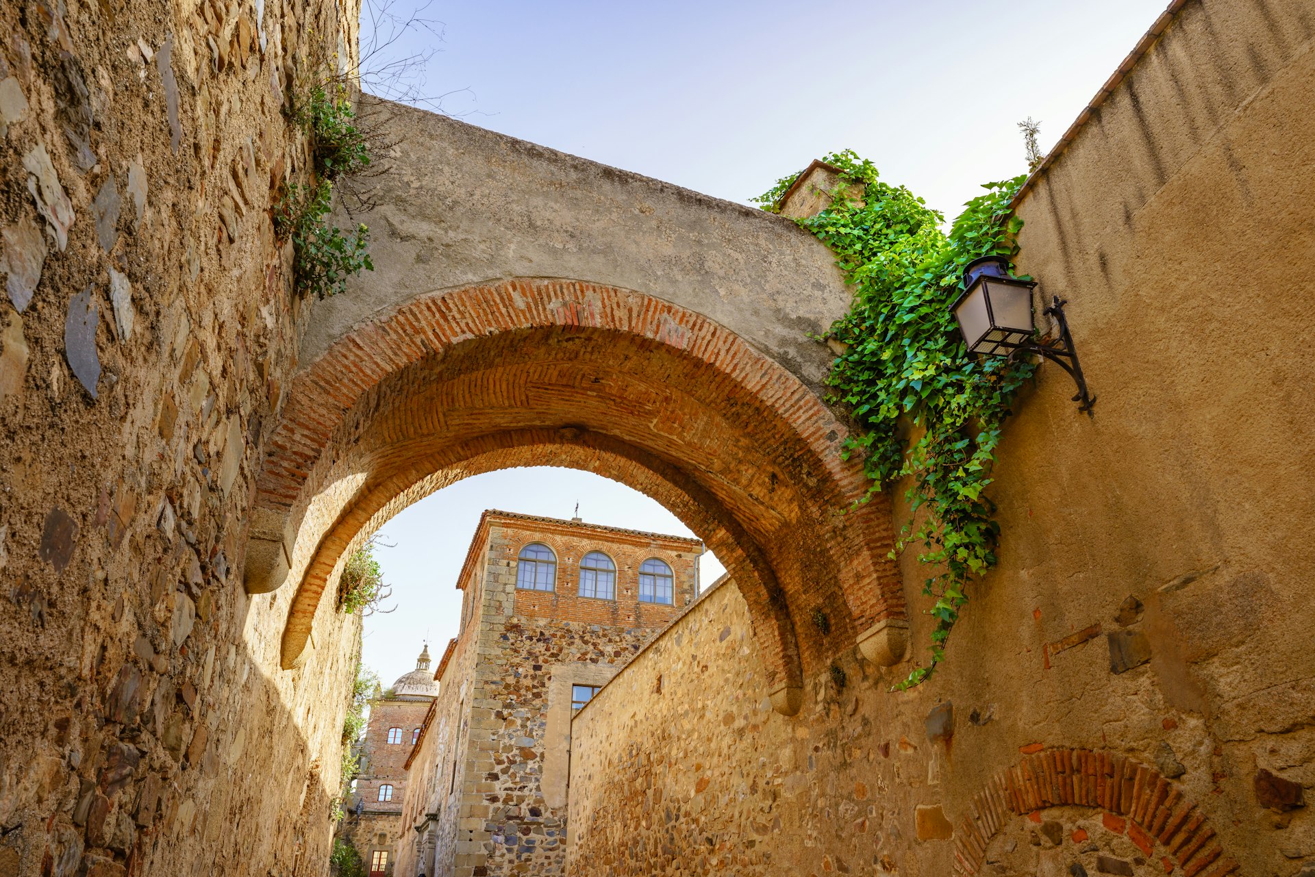 Low angle view of a narrow street under an old arch in Caceres, Extremadura, Spain.