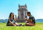 Friends sitting on grass eating a pastel de nata in front of Belem Tower in Lisbon, Portugal
1414092673