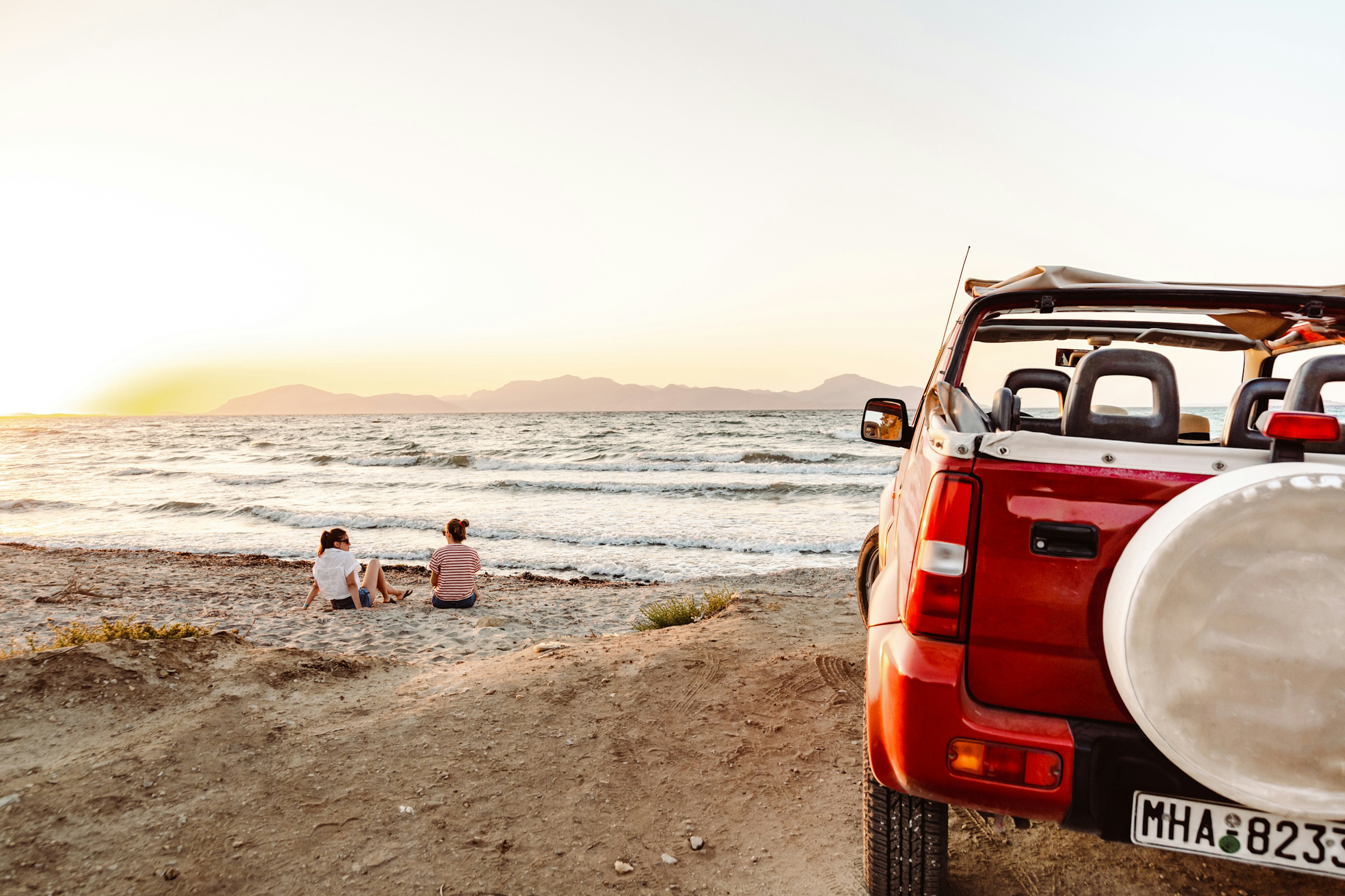 Two women sit on the beach chatting in front of their parked four-wheel drive vehicle