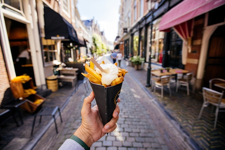 1440601751
A man holds out a cone filled with frites on an Amsterdam street