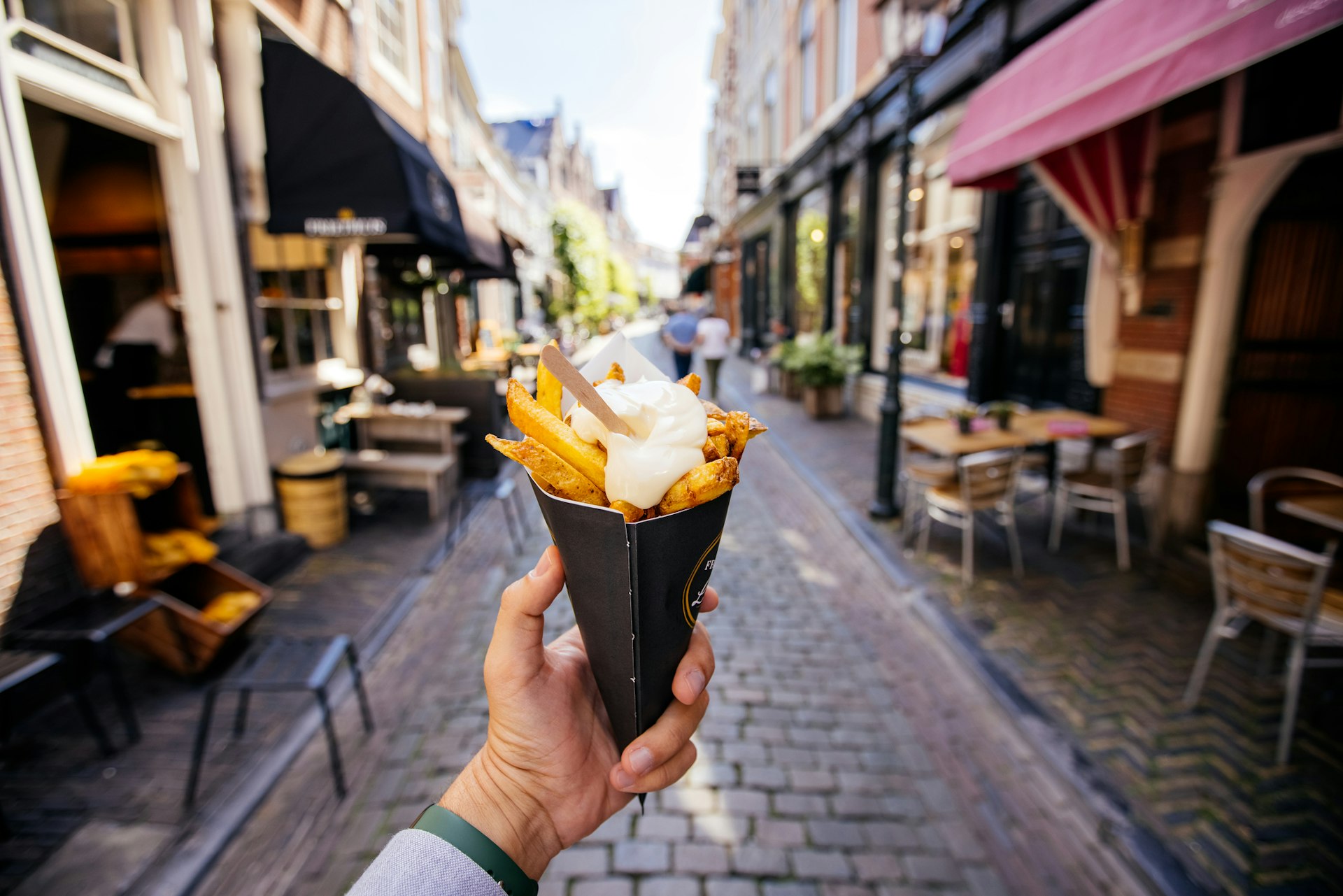 A man holds out a cone filled with frites on an Amsterdam street