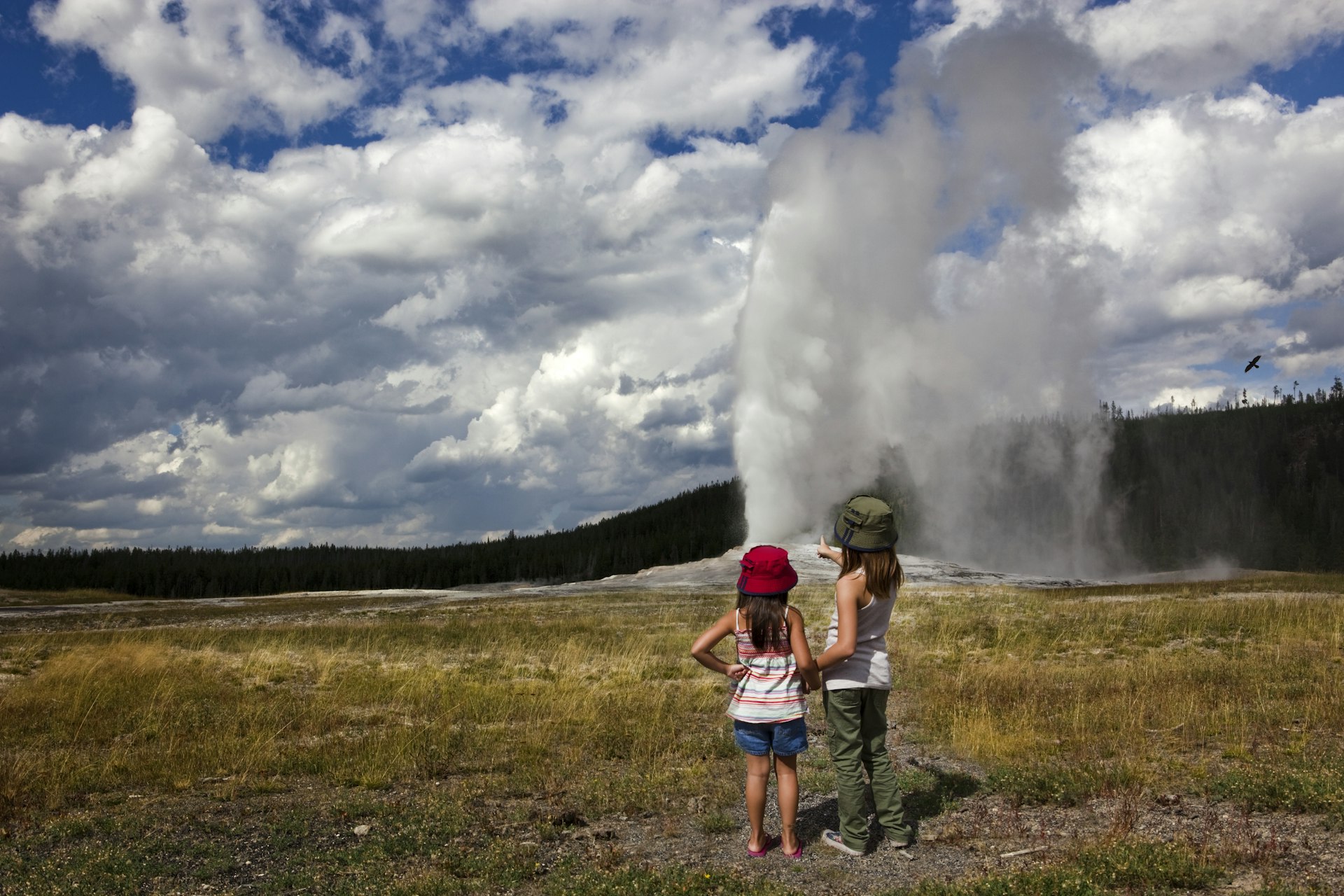 Two young girls watching Old Faithful erupt on a cloudy day