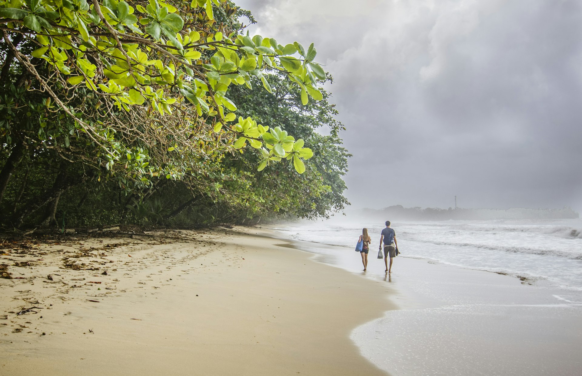 Two people walk along a sandy beach on a stormy day