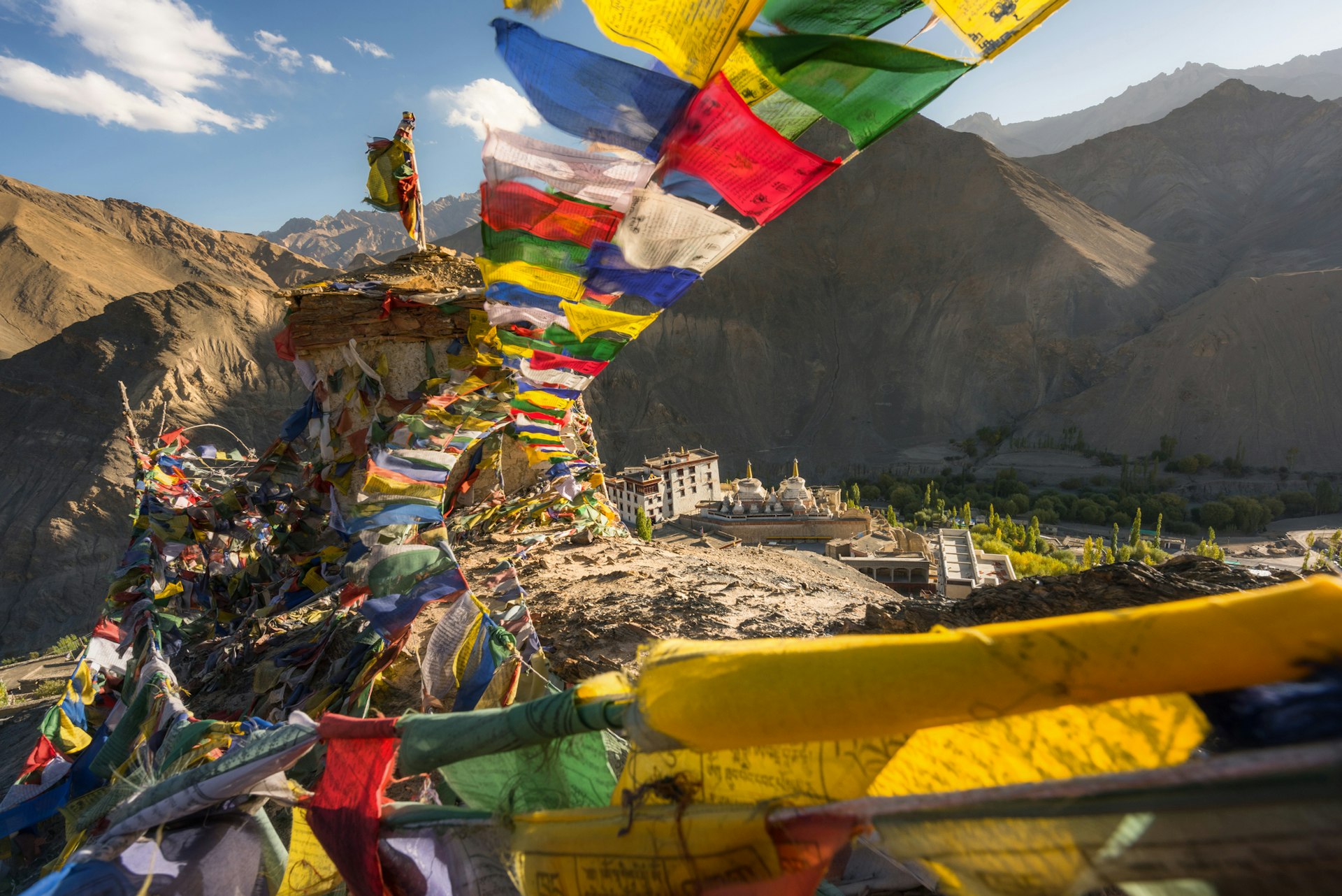 Colorful prayer flags strung high on a mountain top with a monastery in the distance