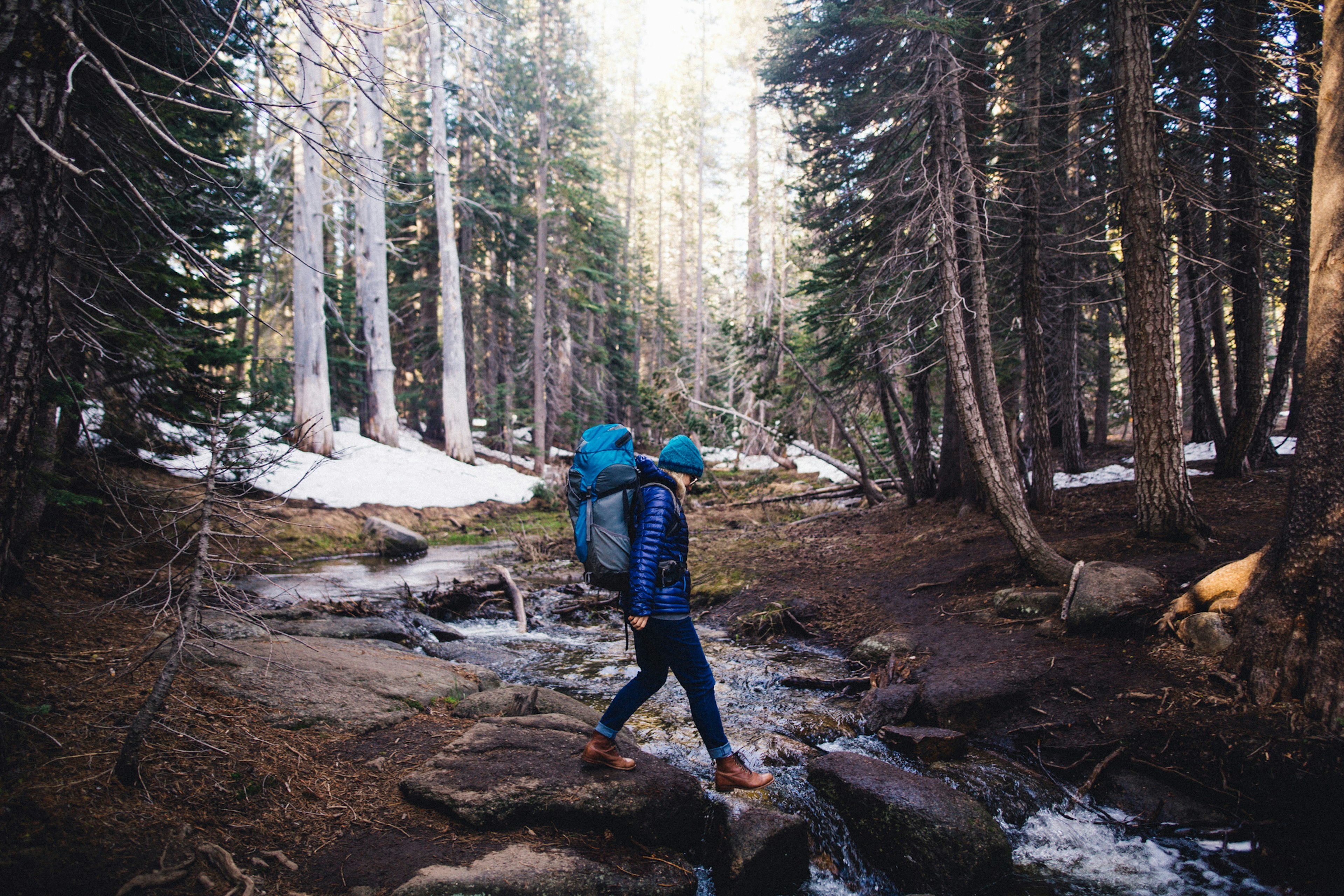 A woman wearing a backpack steps over a stream in Yosemite National Park