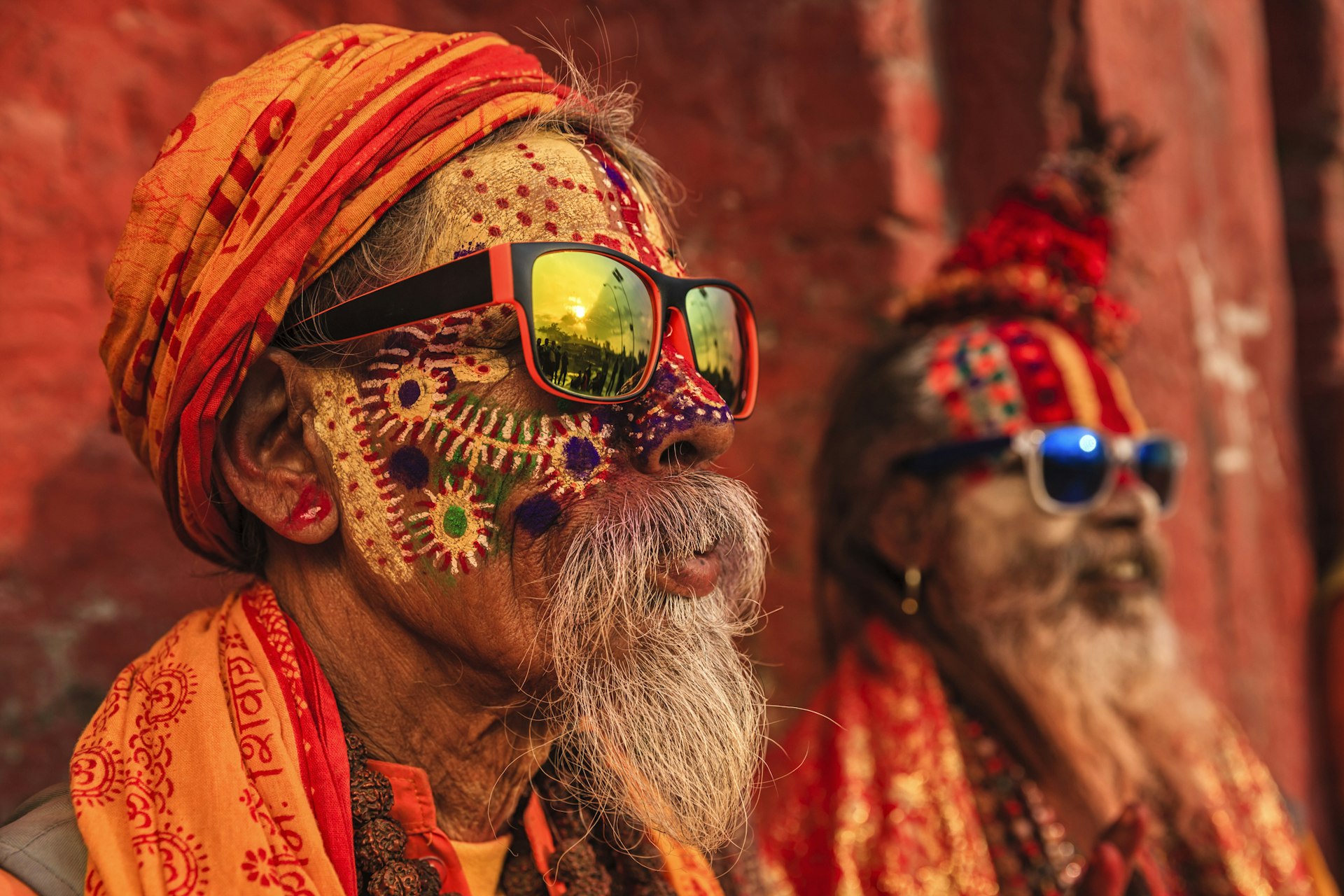 Two Hindu monks wearing brightly colored clothes and painted faces sit in a temple in India