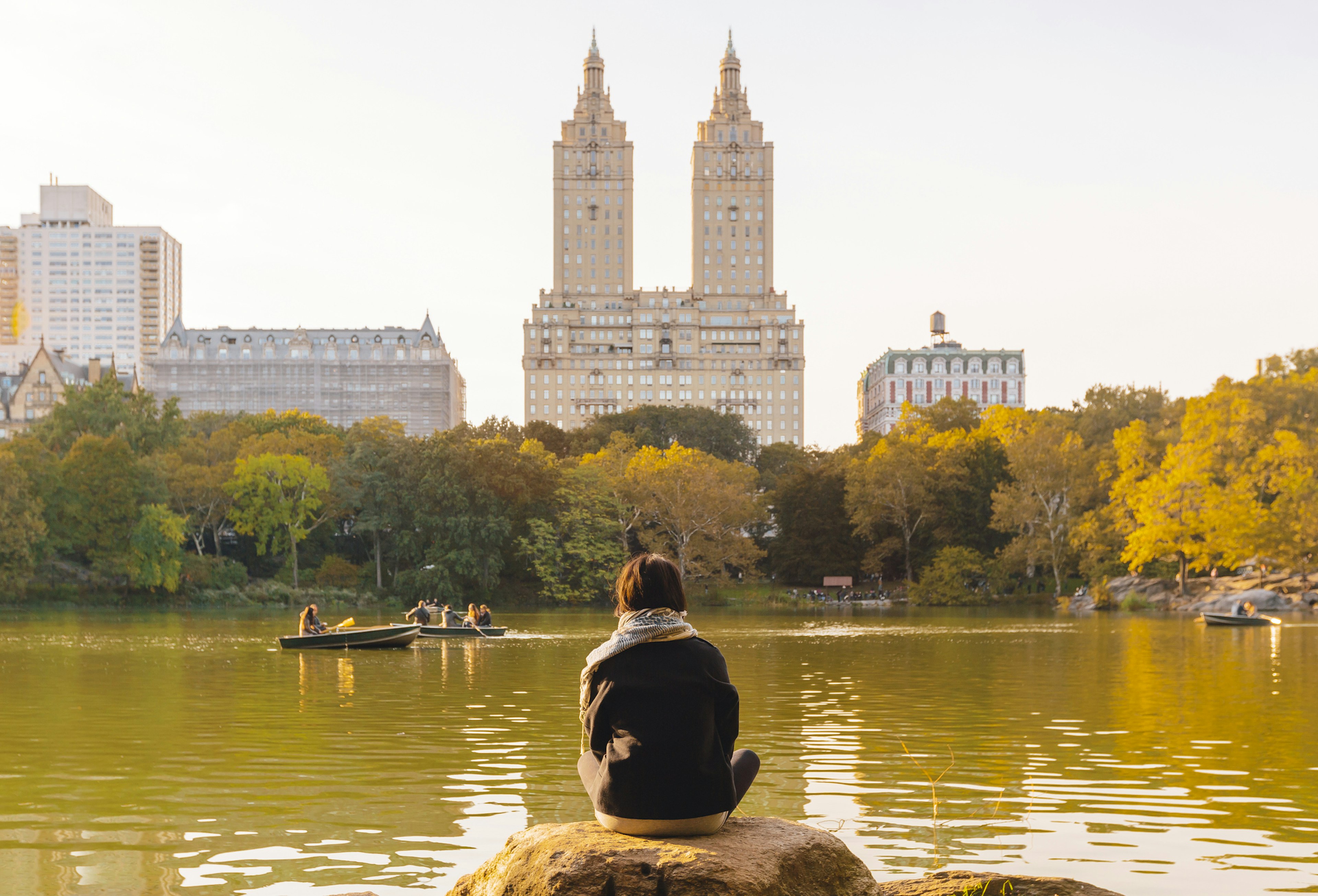 A person sits in front of a lake gazing towards a two-towered apartment block