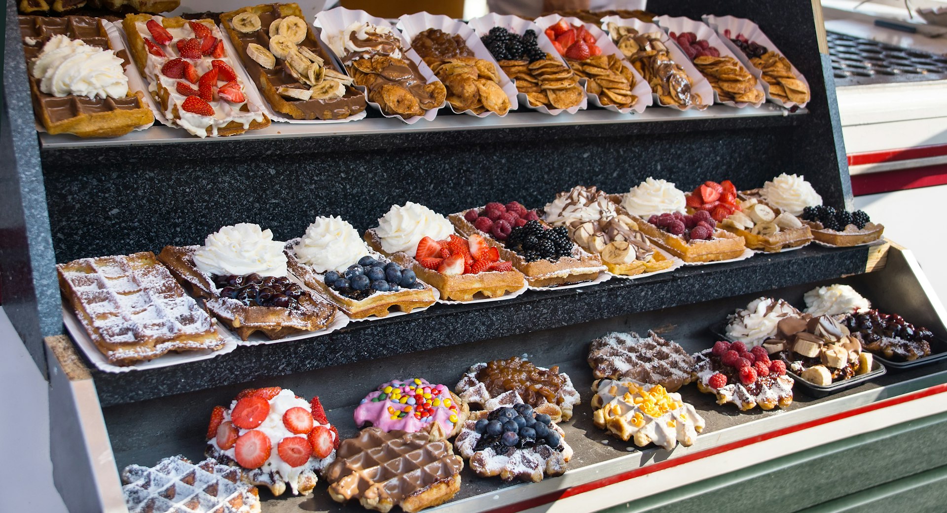 A display of waffles covered in many different toppings including fruit, cream and chocolate sauce