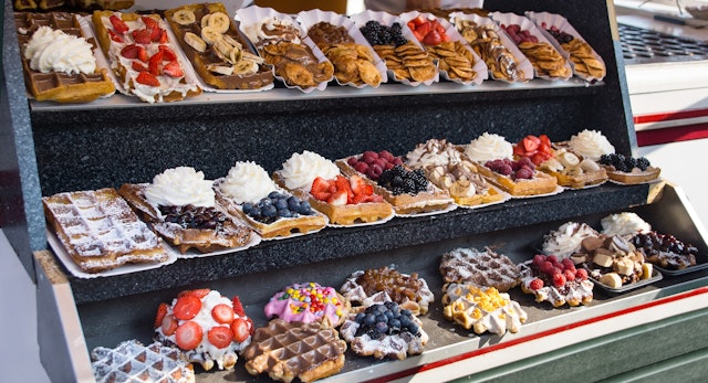 A display of waffles covered in many different toppings including fruit, cream and chocolate sauce