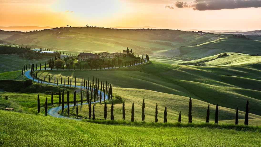 Sunset over a winding road with cypresses in Tuscany.