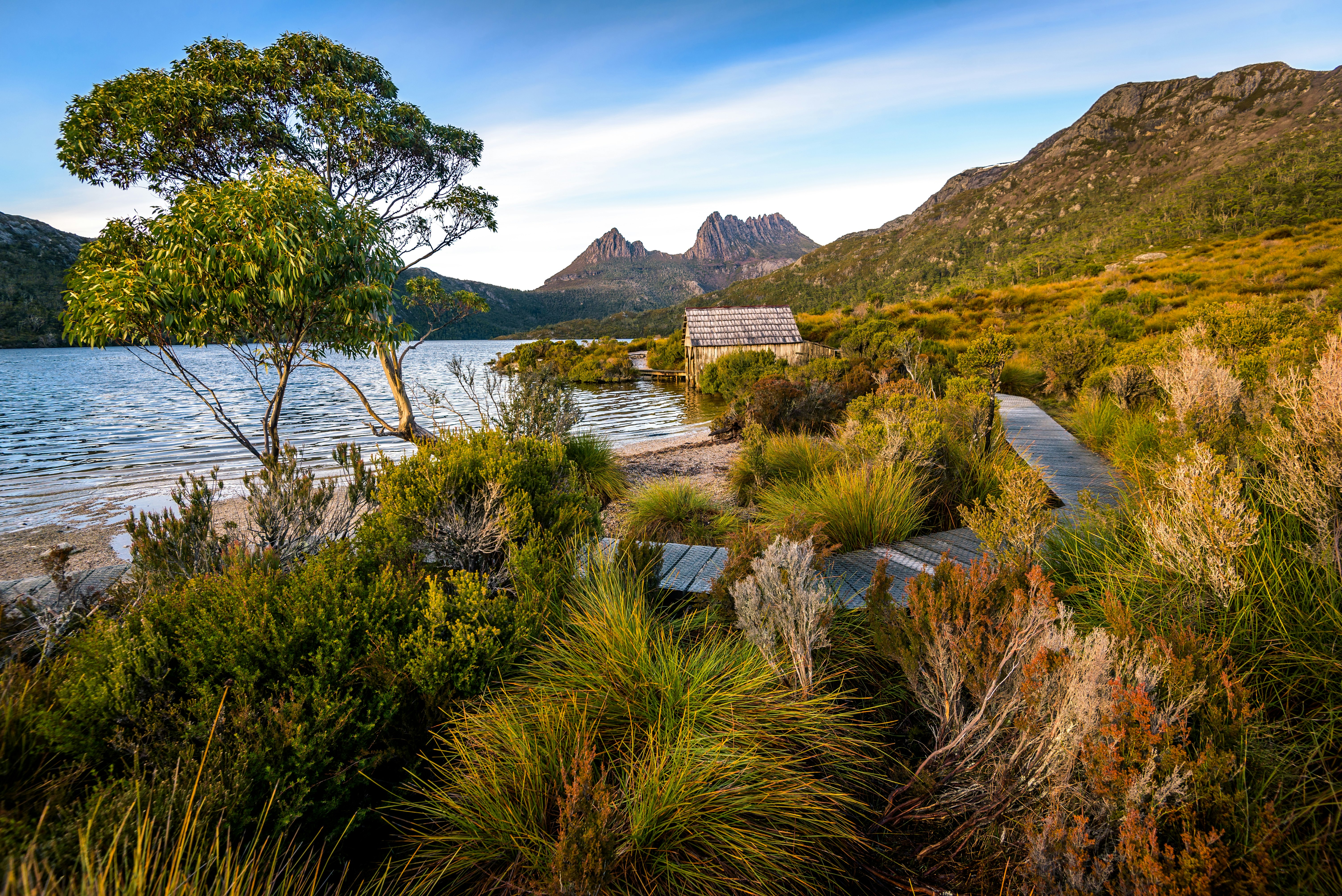 A boardwalk runs along a lake leading to a small wooden boathouse