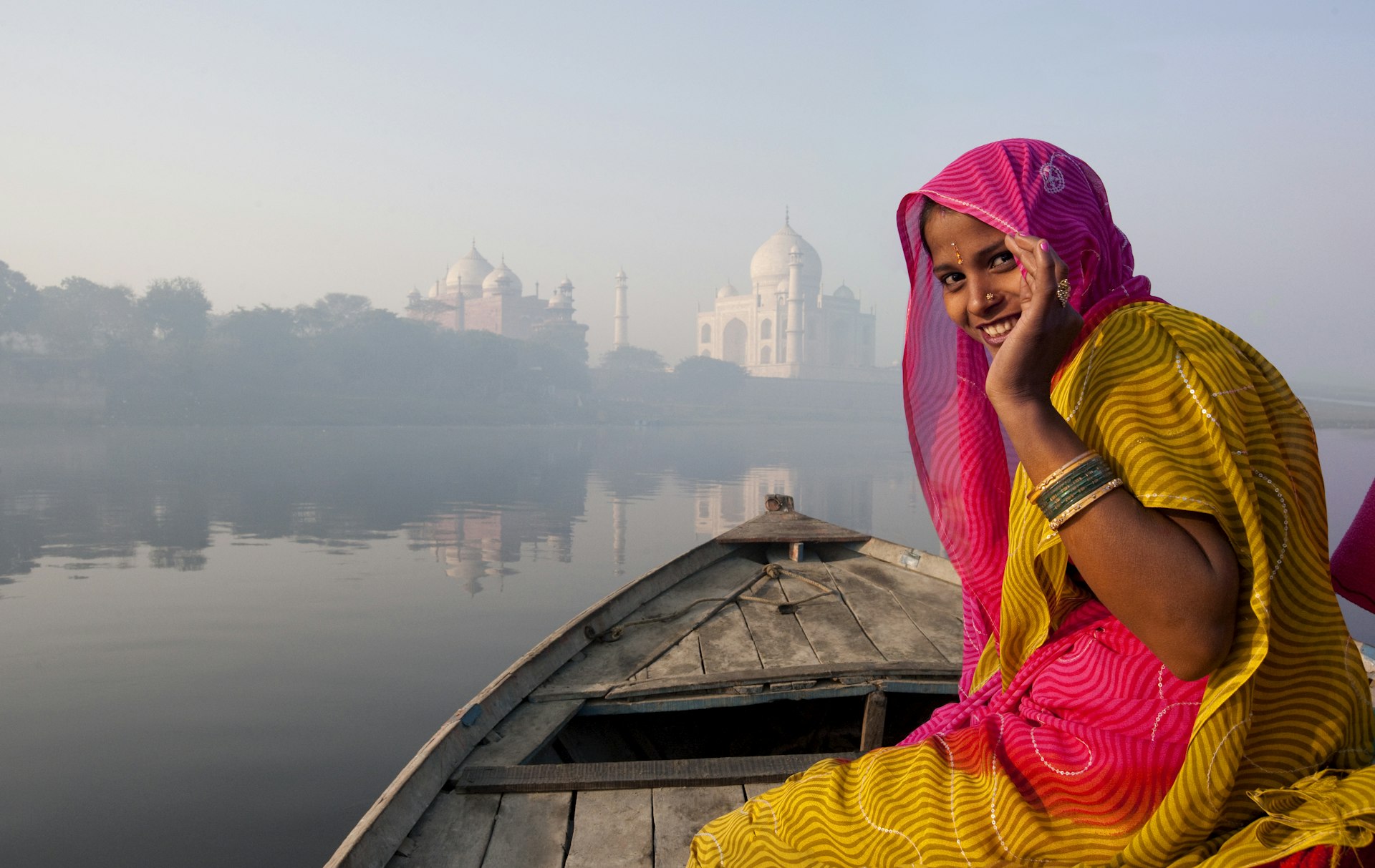 A woman in traditional Indian dress smiles as she rides in a boat towards the epic white marble Taj Mahal