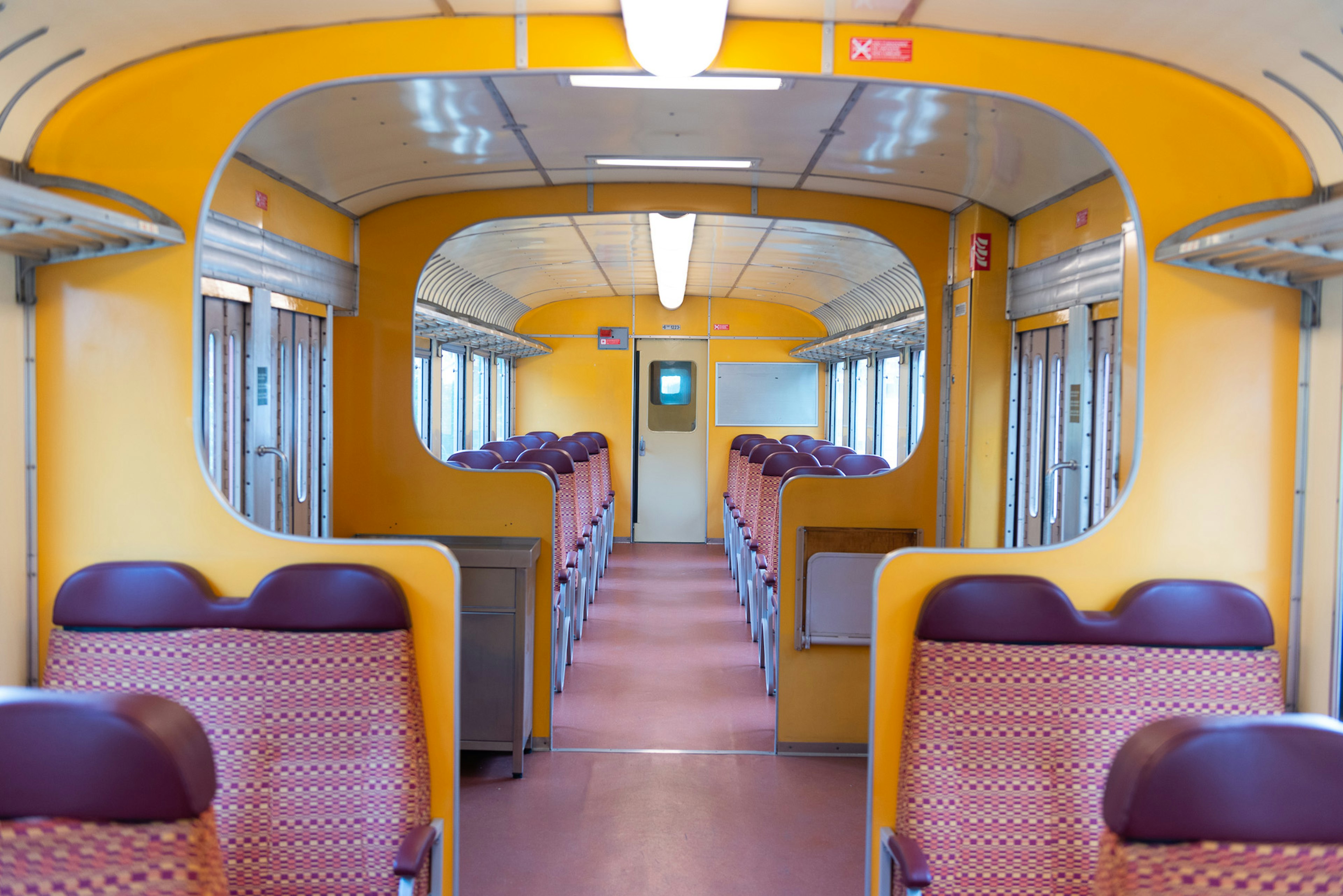 The retro interior of an empty train carriage, with symmetrical seats and decor