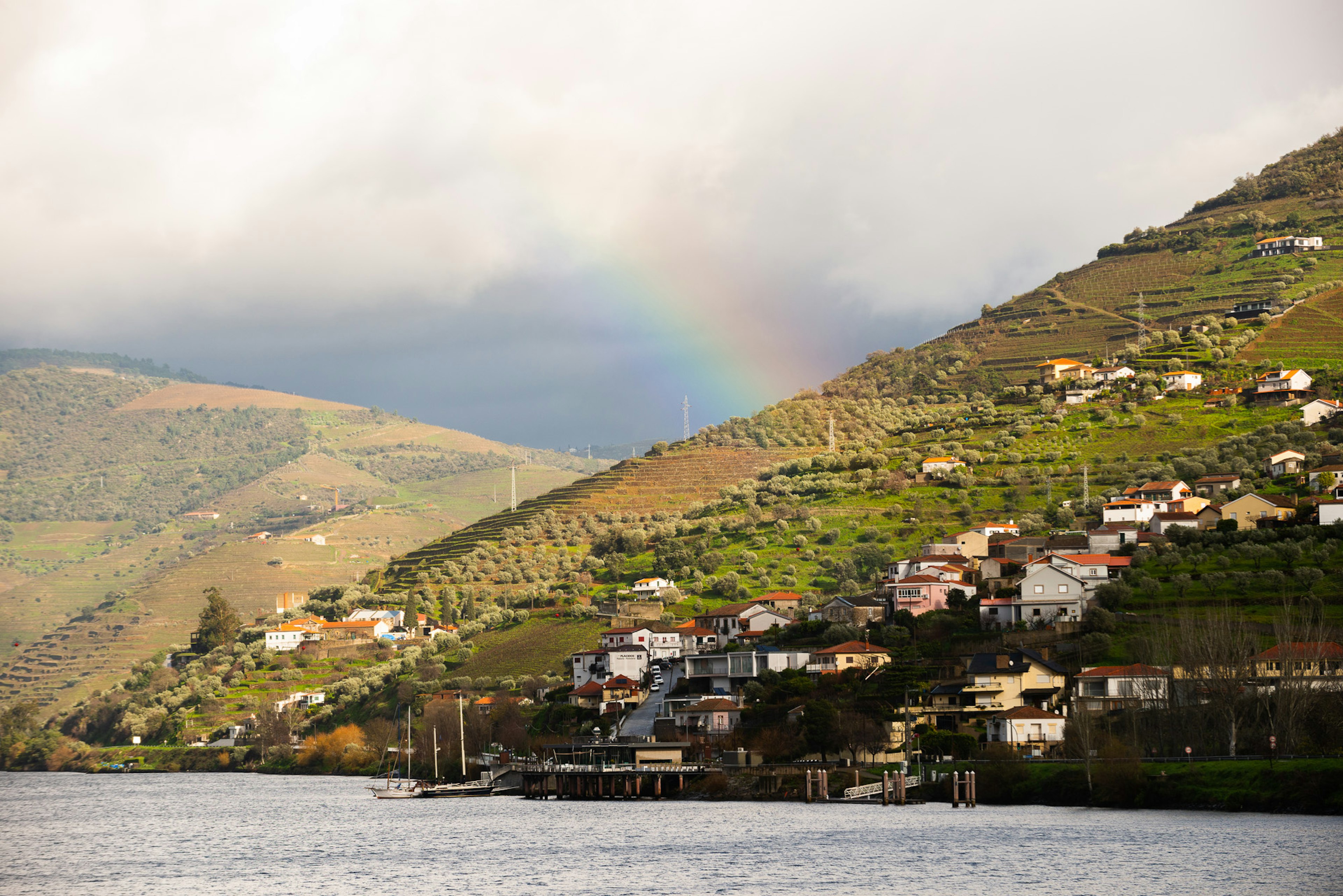 A rainbow over a riverside village and vineyards