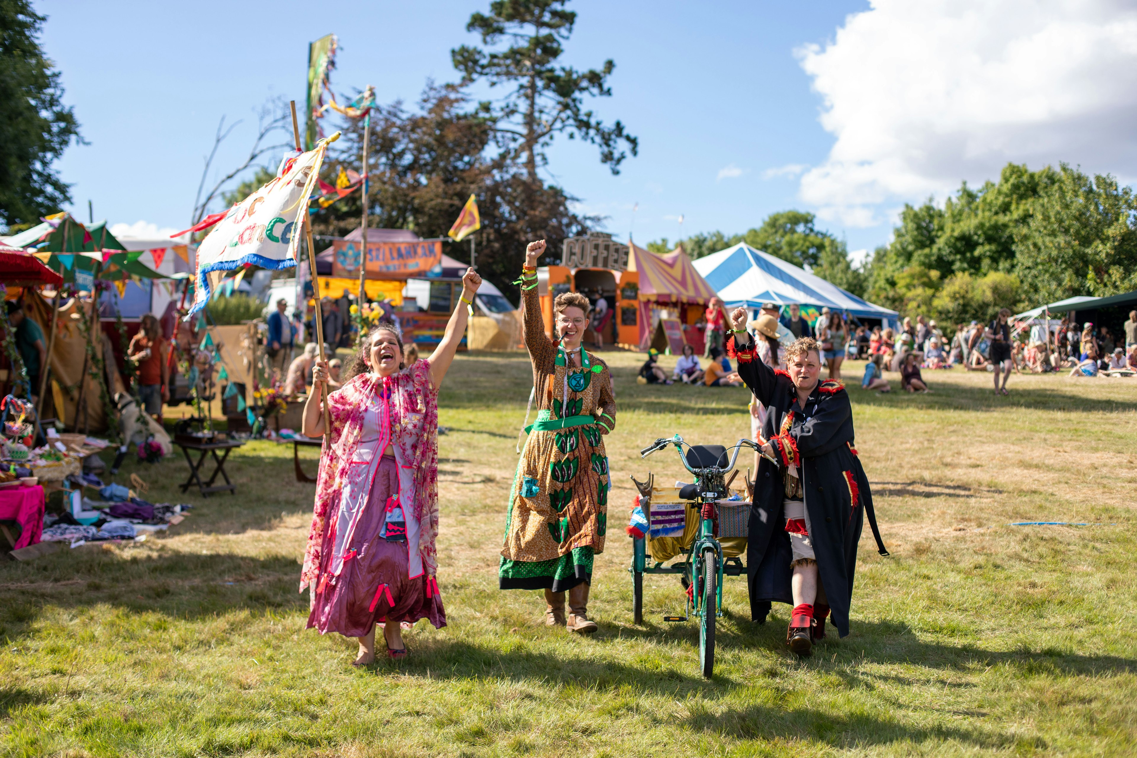 Festival goers surrounded by colorful tents and flags in a field enjoying the Green Gathering festival, Wales