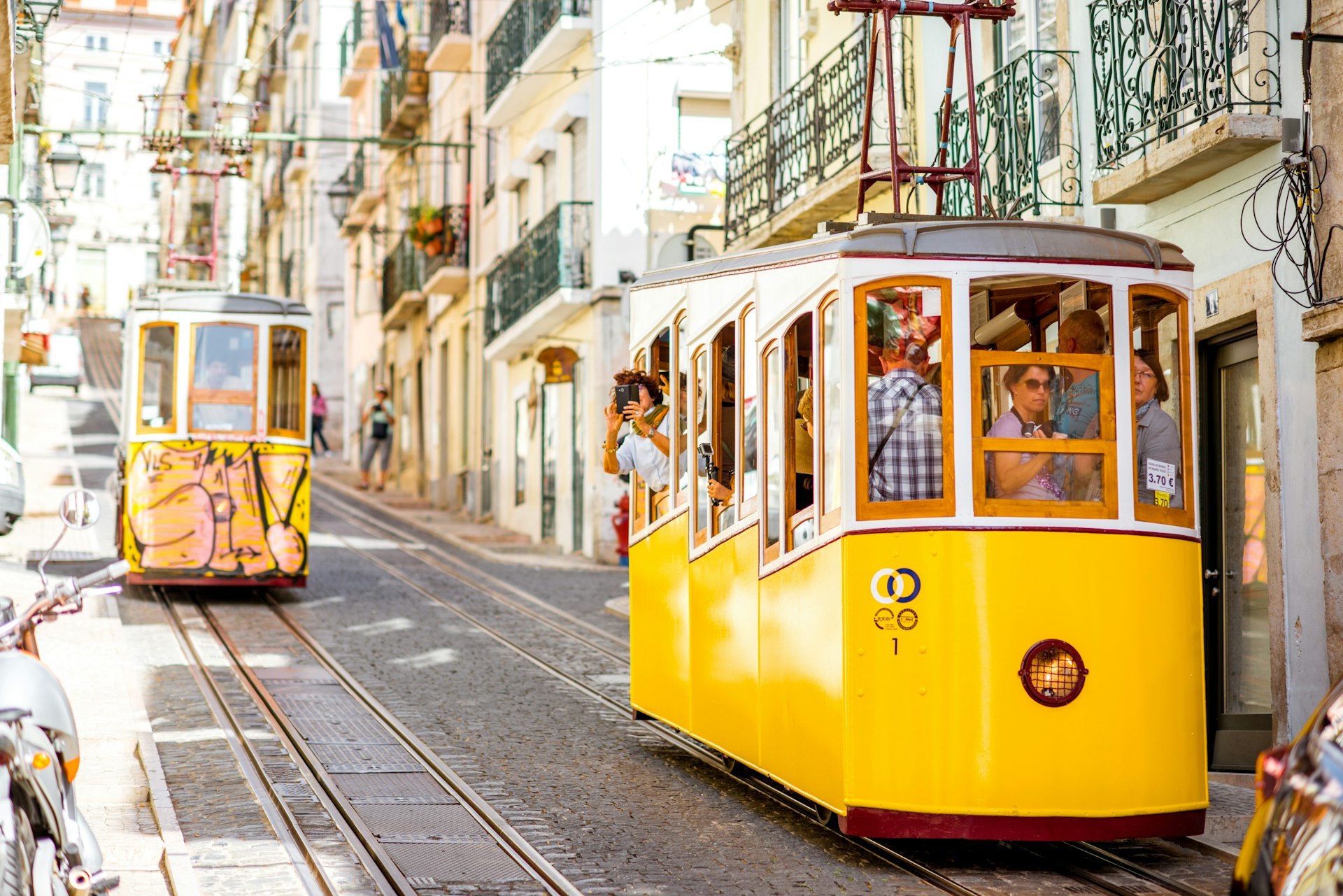 Two yellow trams traveling down a steep cobbled street in Lisbon