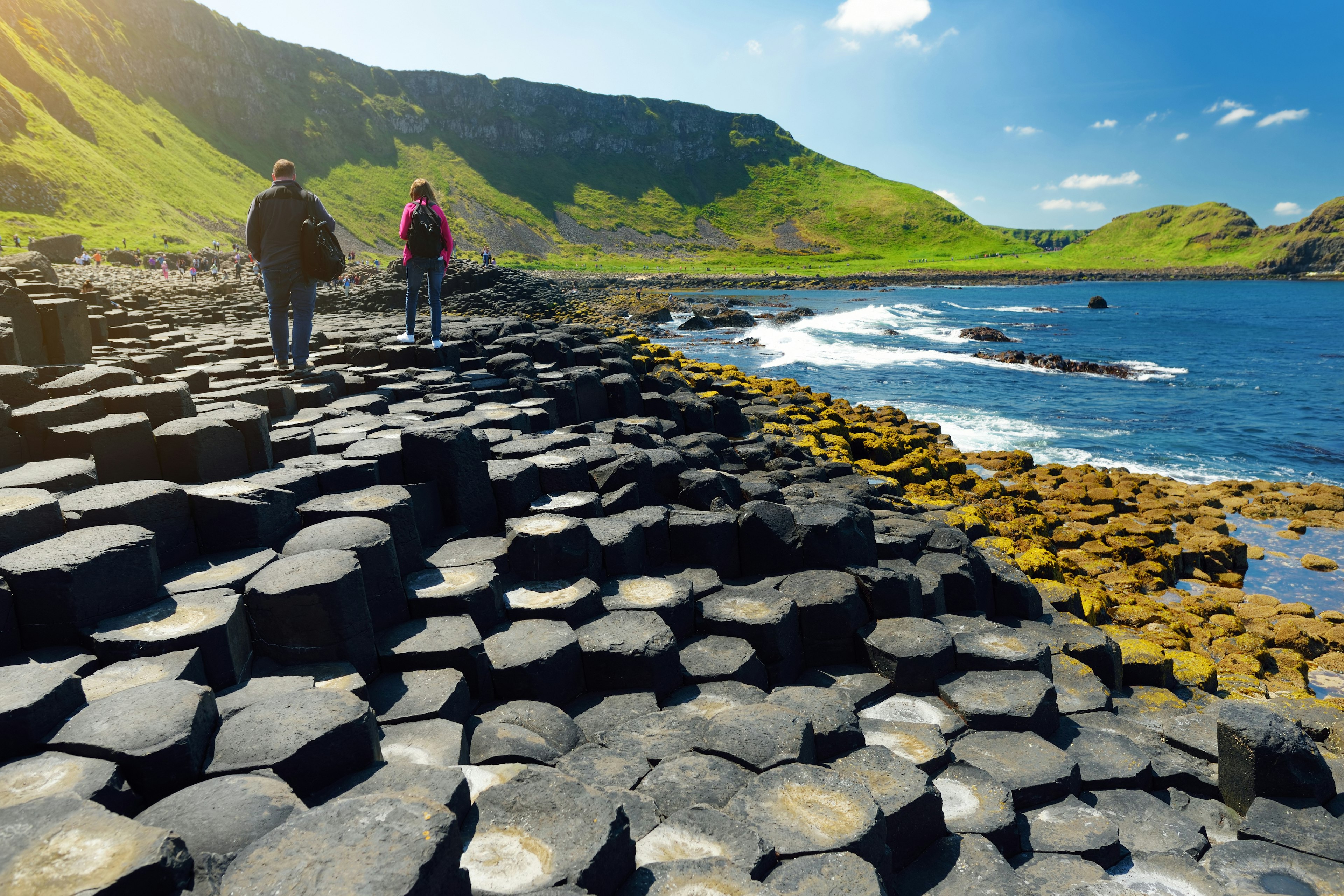 Tourists walking at Giants Causeway, an area of hexagonal basalt stones, created by ancient volcanic fissure eruption, County Antrim, Northern Ireland.