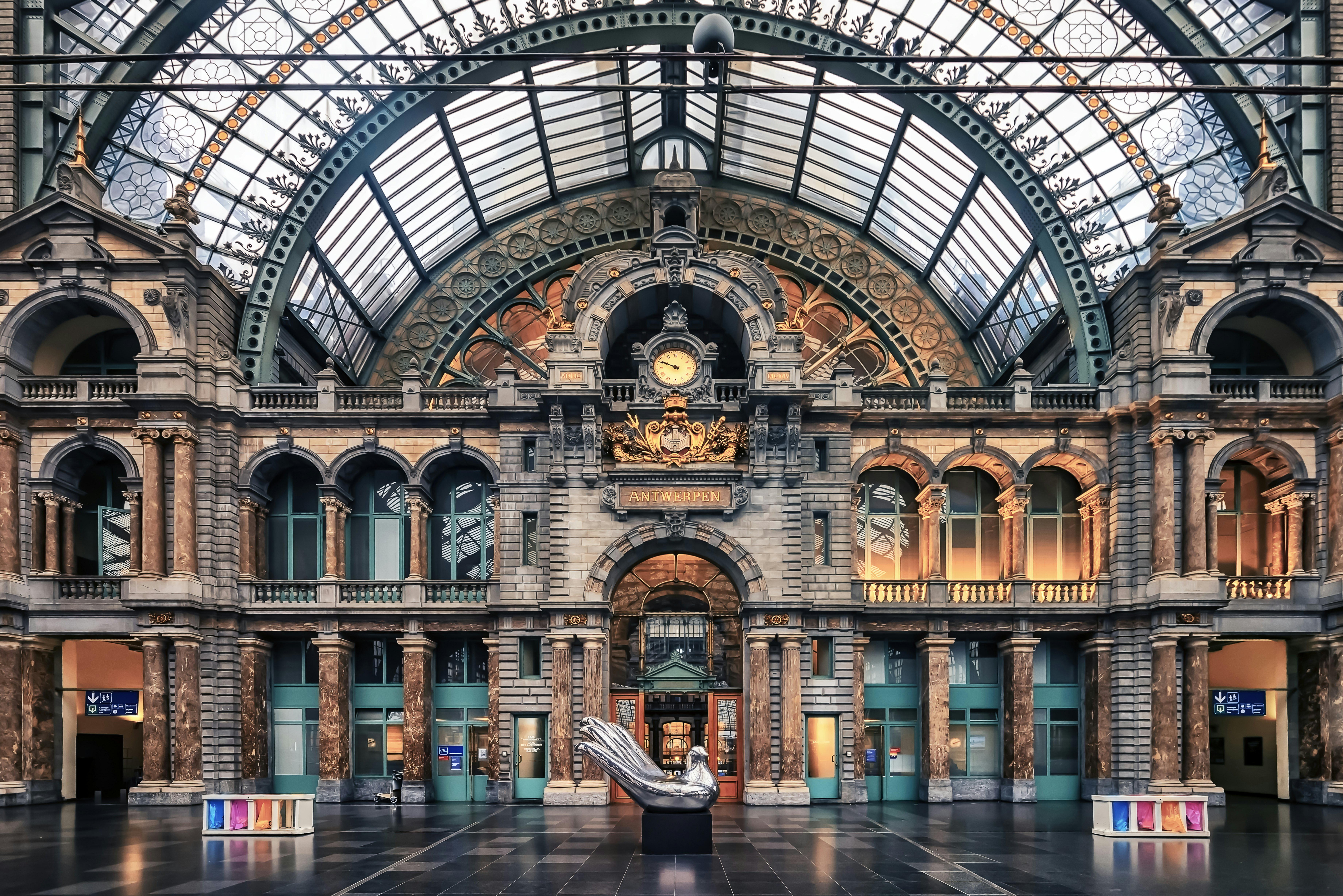 The interior of a grand station with a clock, glass ceiling and ornate windows