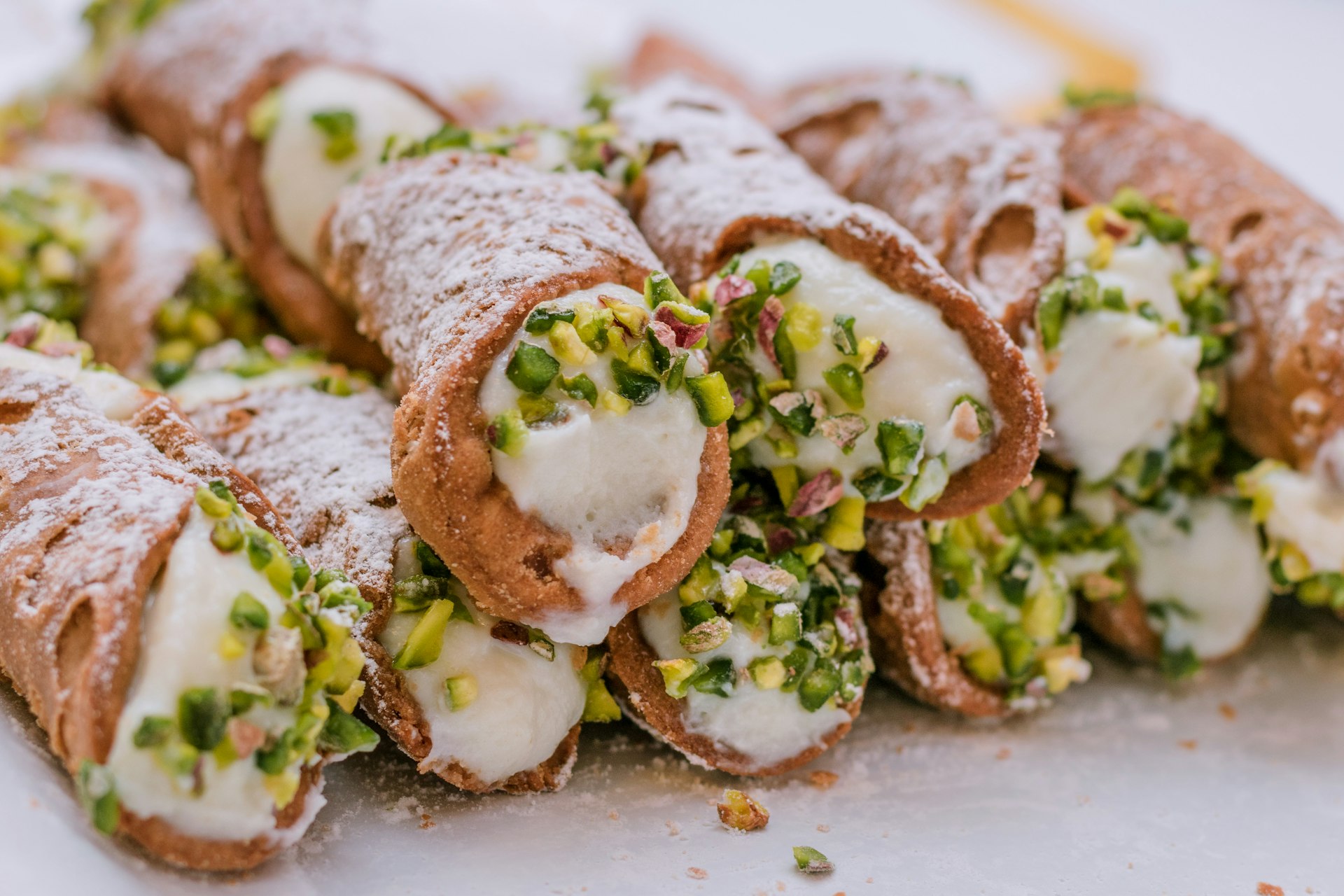 A close-up of a pile of Sicilian cannoli, tubular pastry shells filled with pistachio-studded ricotta and covered with powdered sugar
