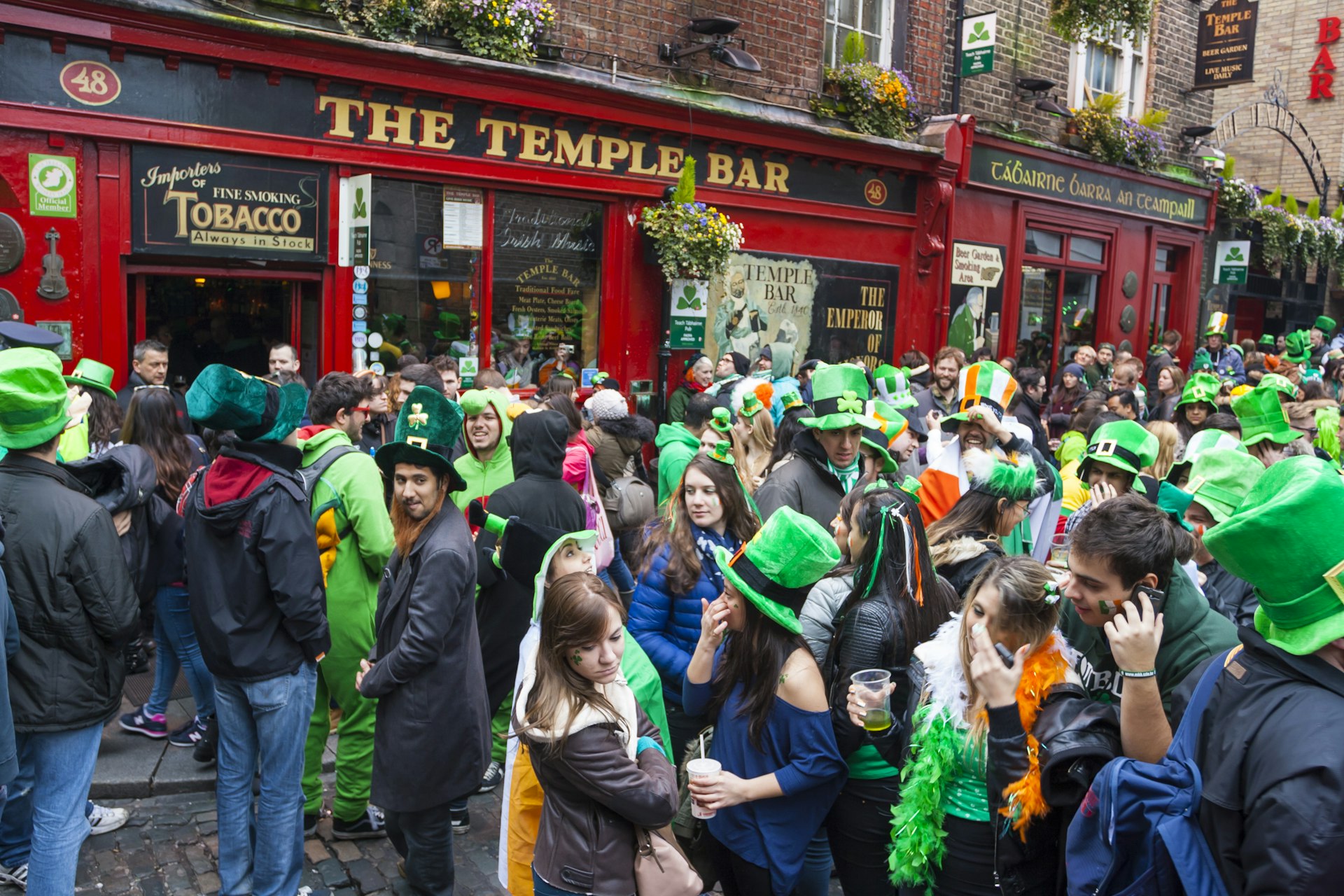 Crowds gather outside a pub named Temple Bar all dressed in oversized green hats to celebrate St Patrick's Day