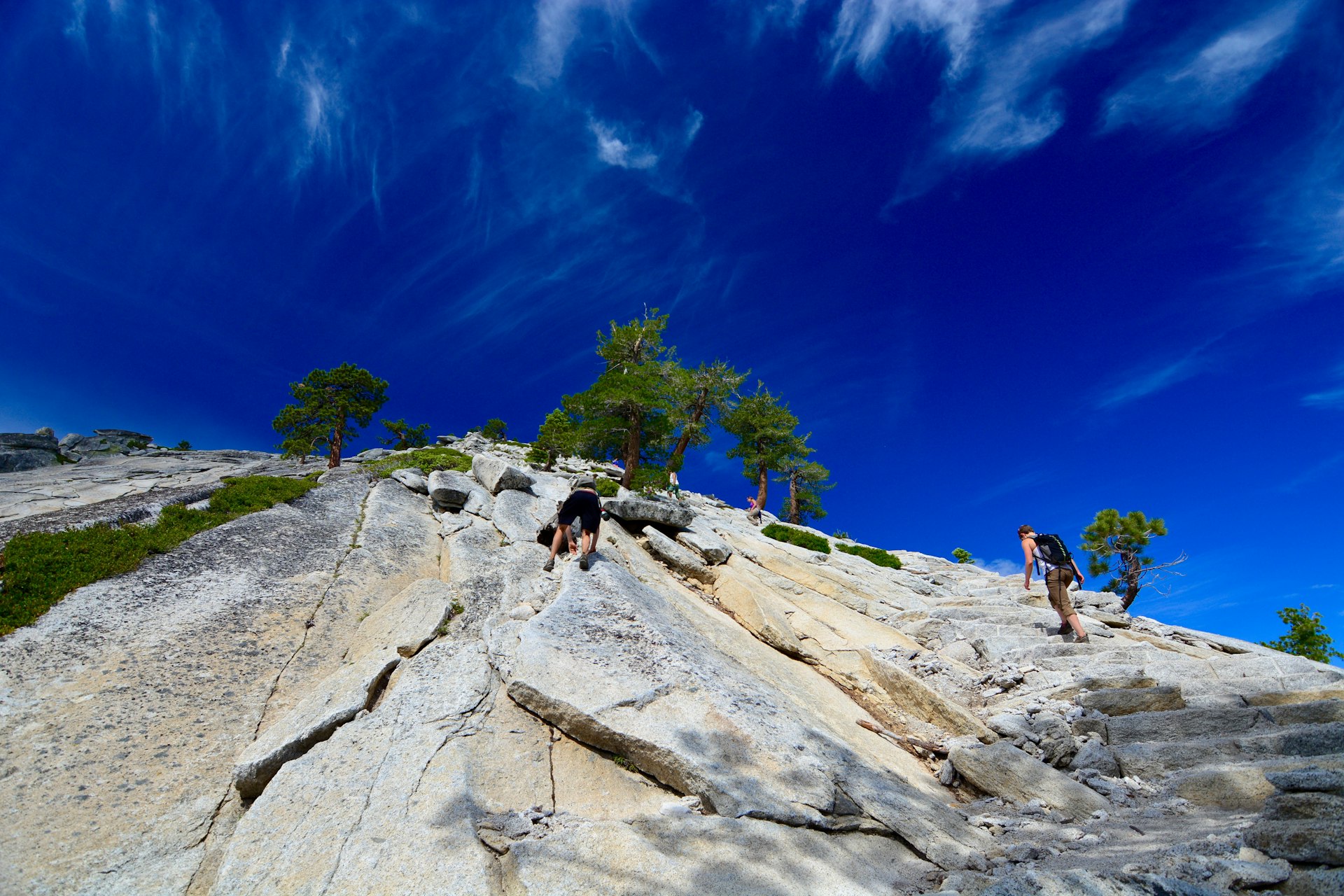 Hikers climbing Yosemite's rocky Half Dome on a sunny day