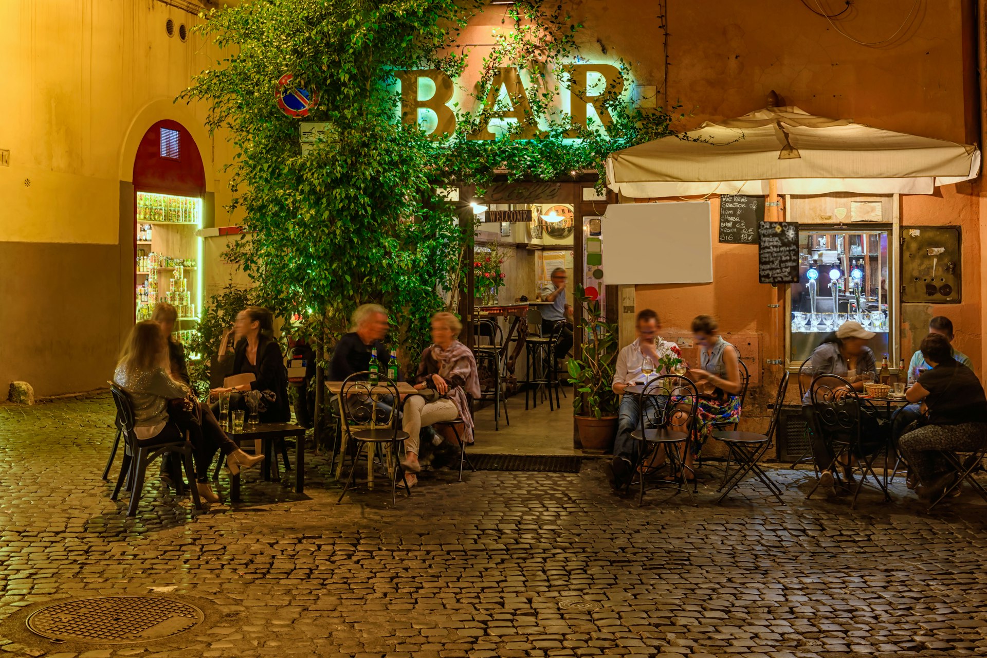 People sit outside a bar on an old street at night in Trastevere, Rome