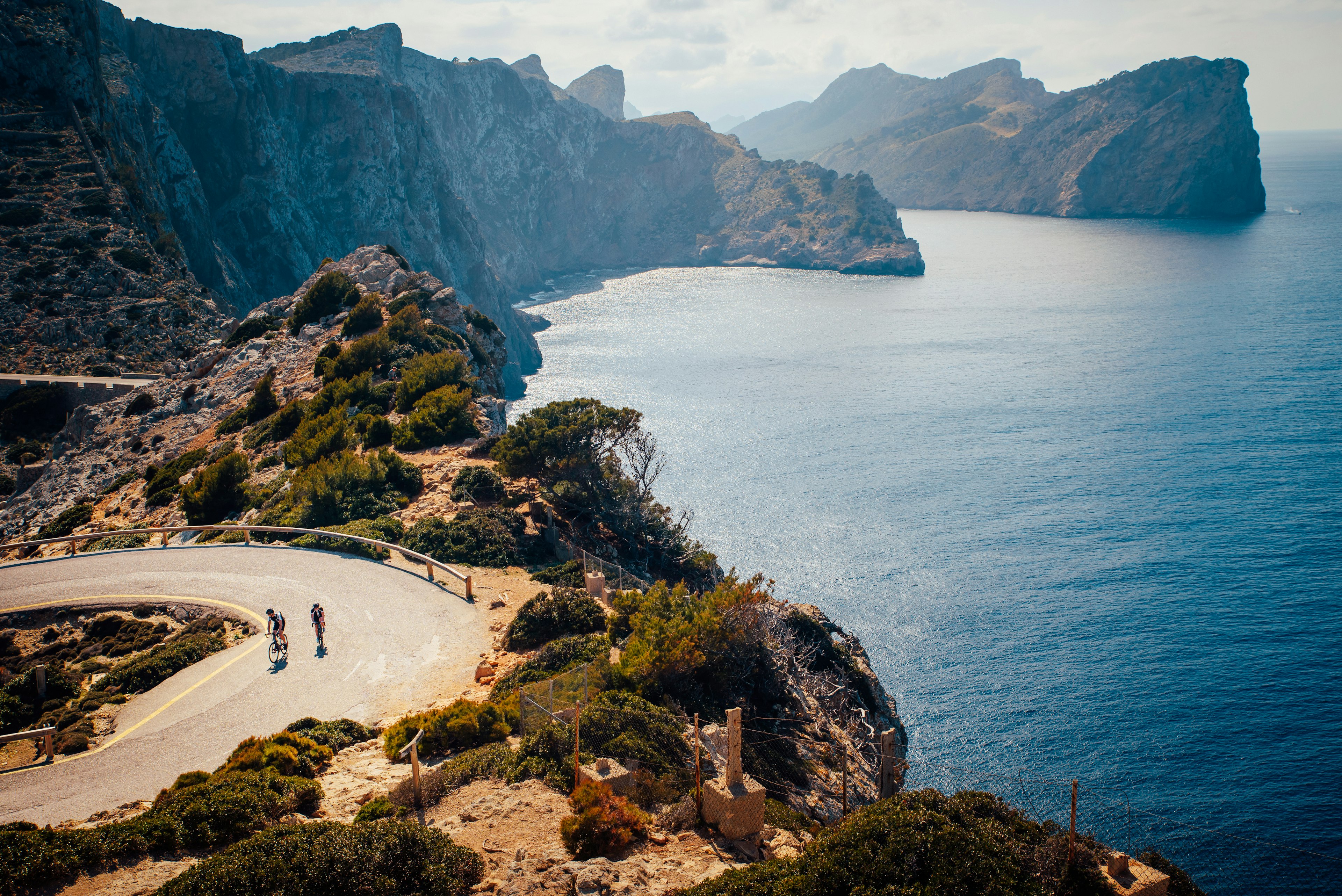 A couple of people cycle on a cliffside road in Mallorca.