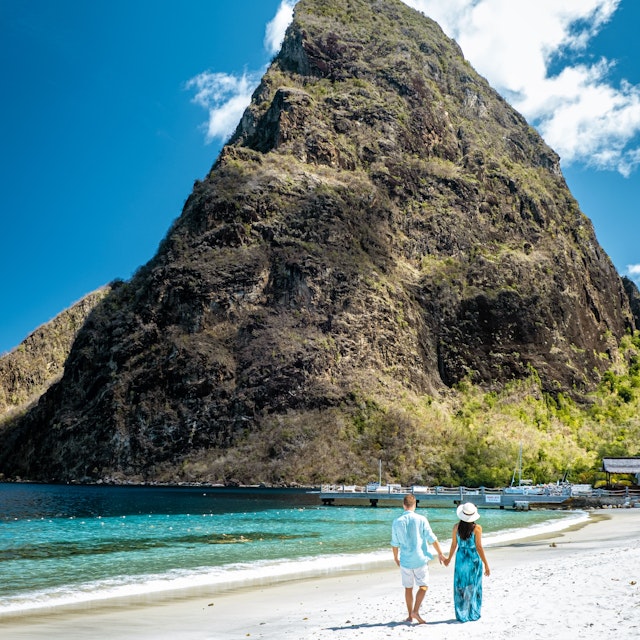 A couple walks on a beach in front of Gros Piton, St Lucia, Caribbean