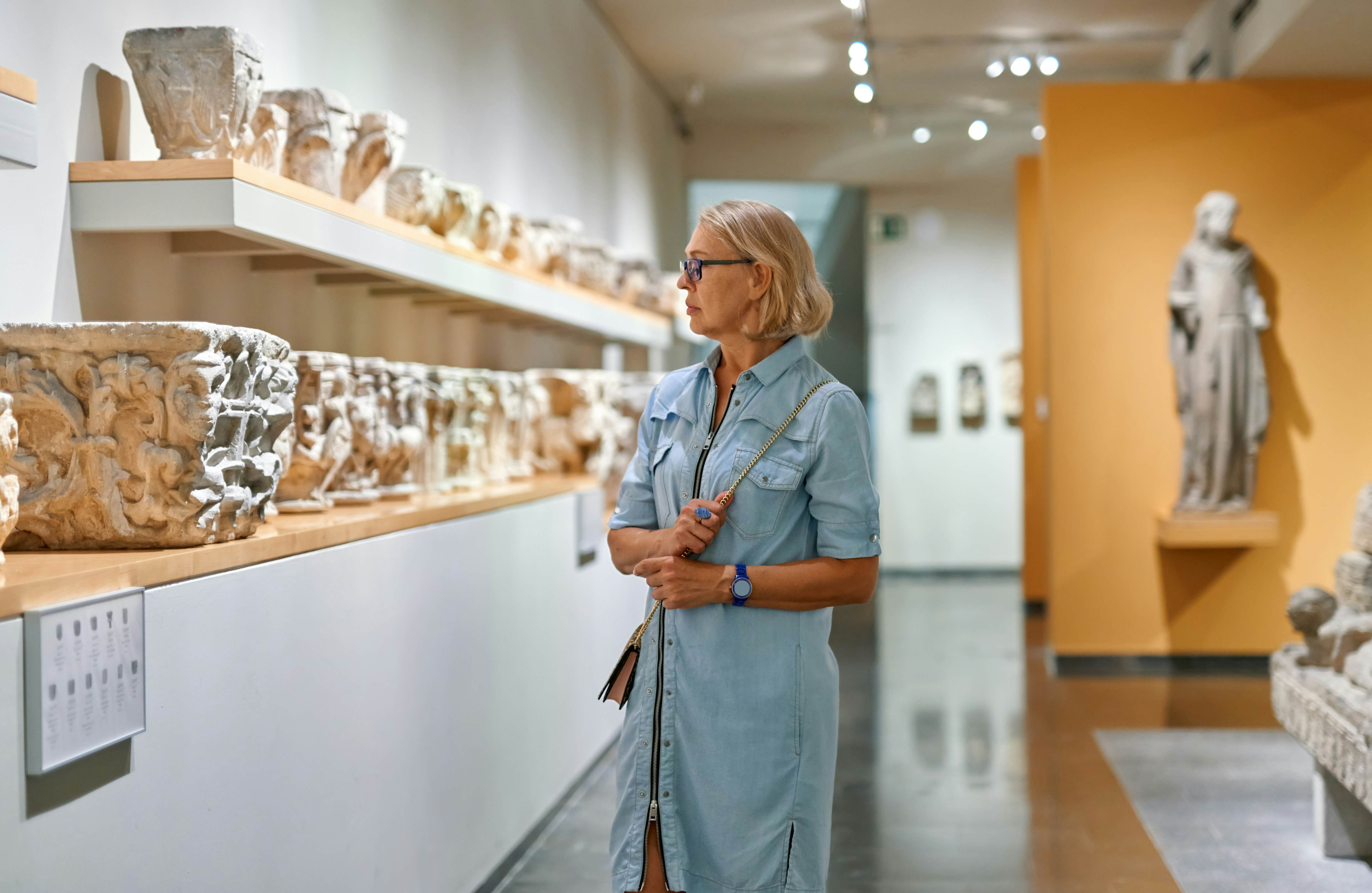 A woman looks at ancient Greek sculptures that line the walls of a museum