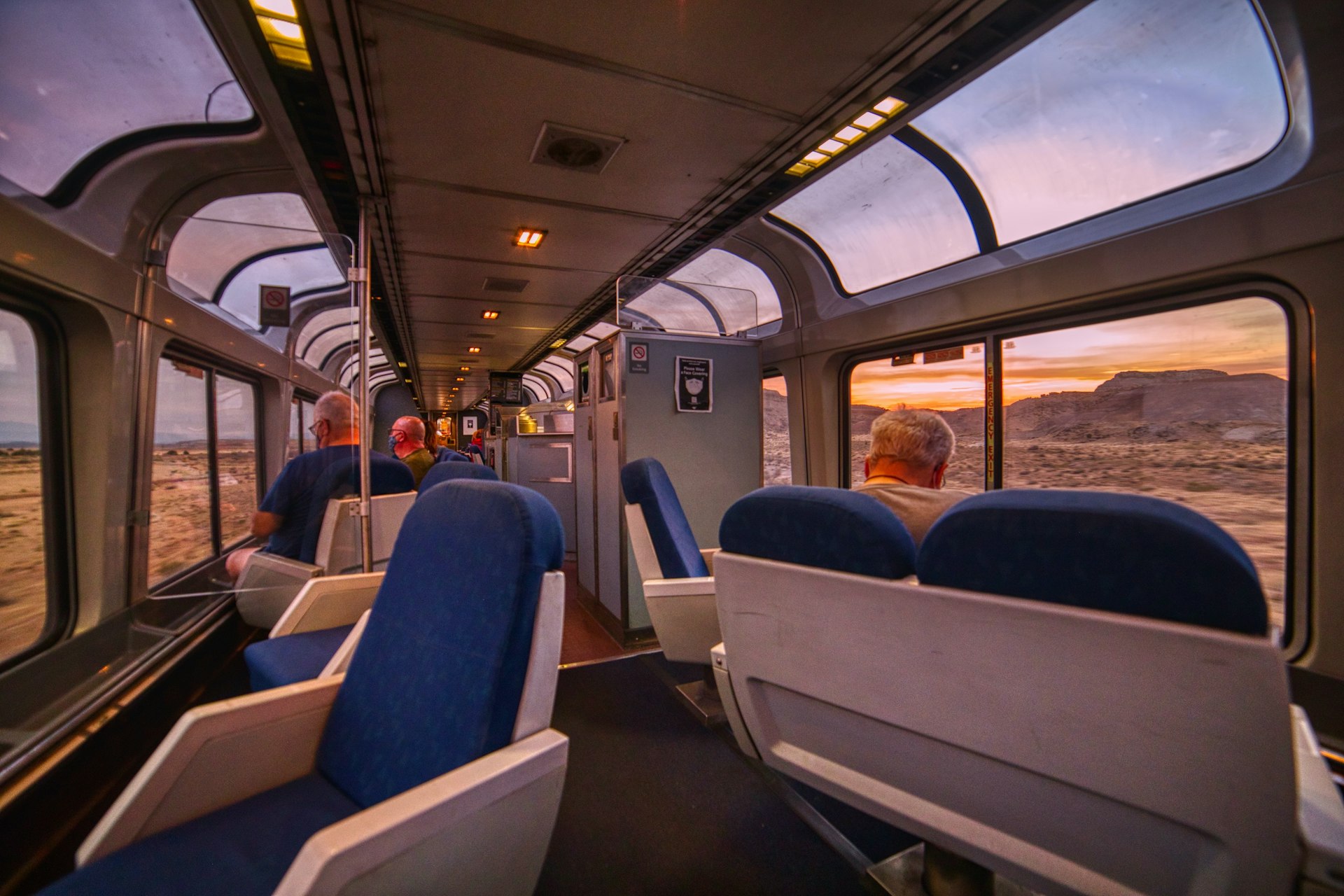People sit in an observation train car looking out at the sunset on an Amtrak train, USA