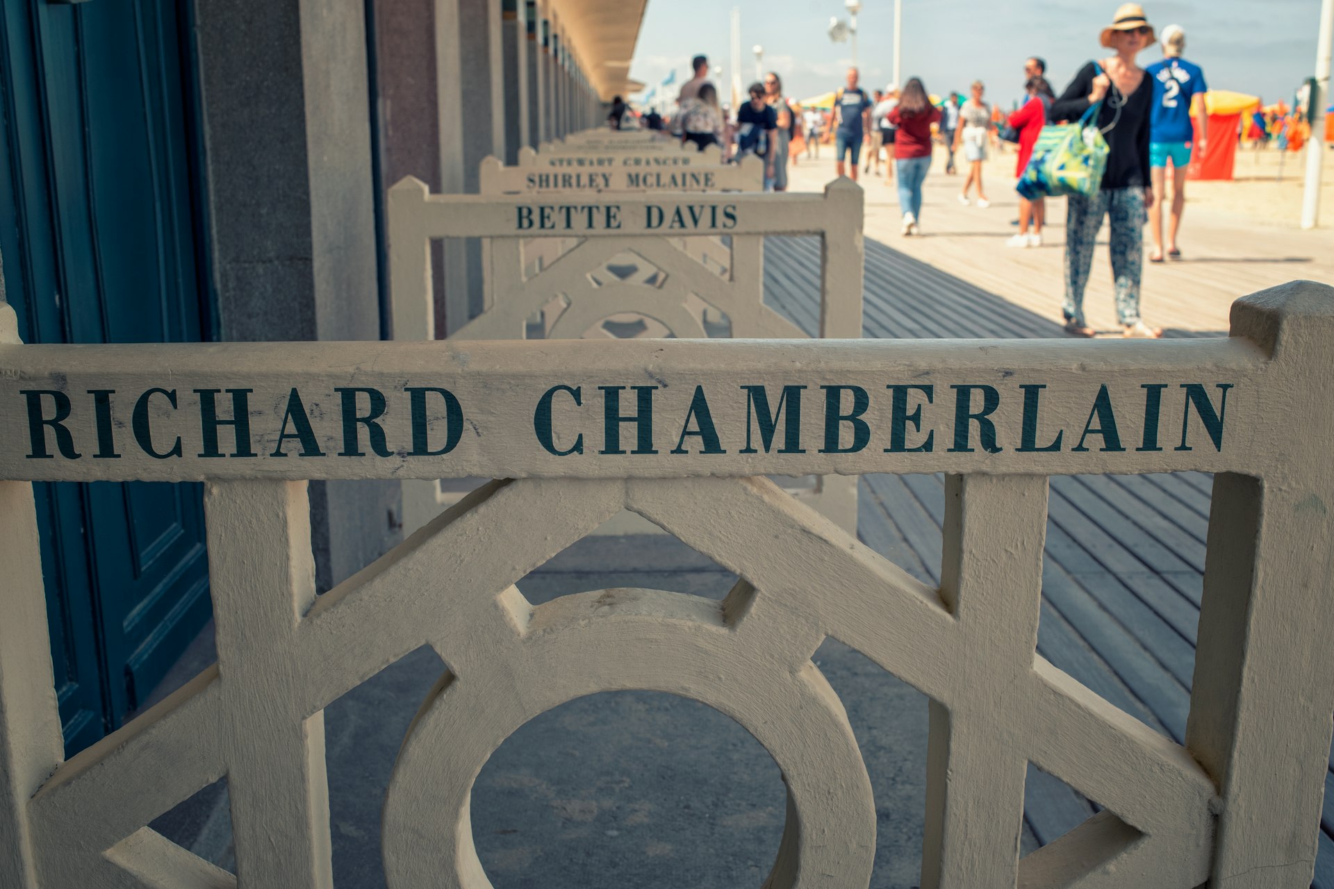 A close-up of a wooden barrier with the name Richard Chamberlain on it outside an art deco beach hut on a boardwalk by the sand