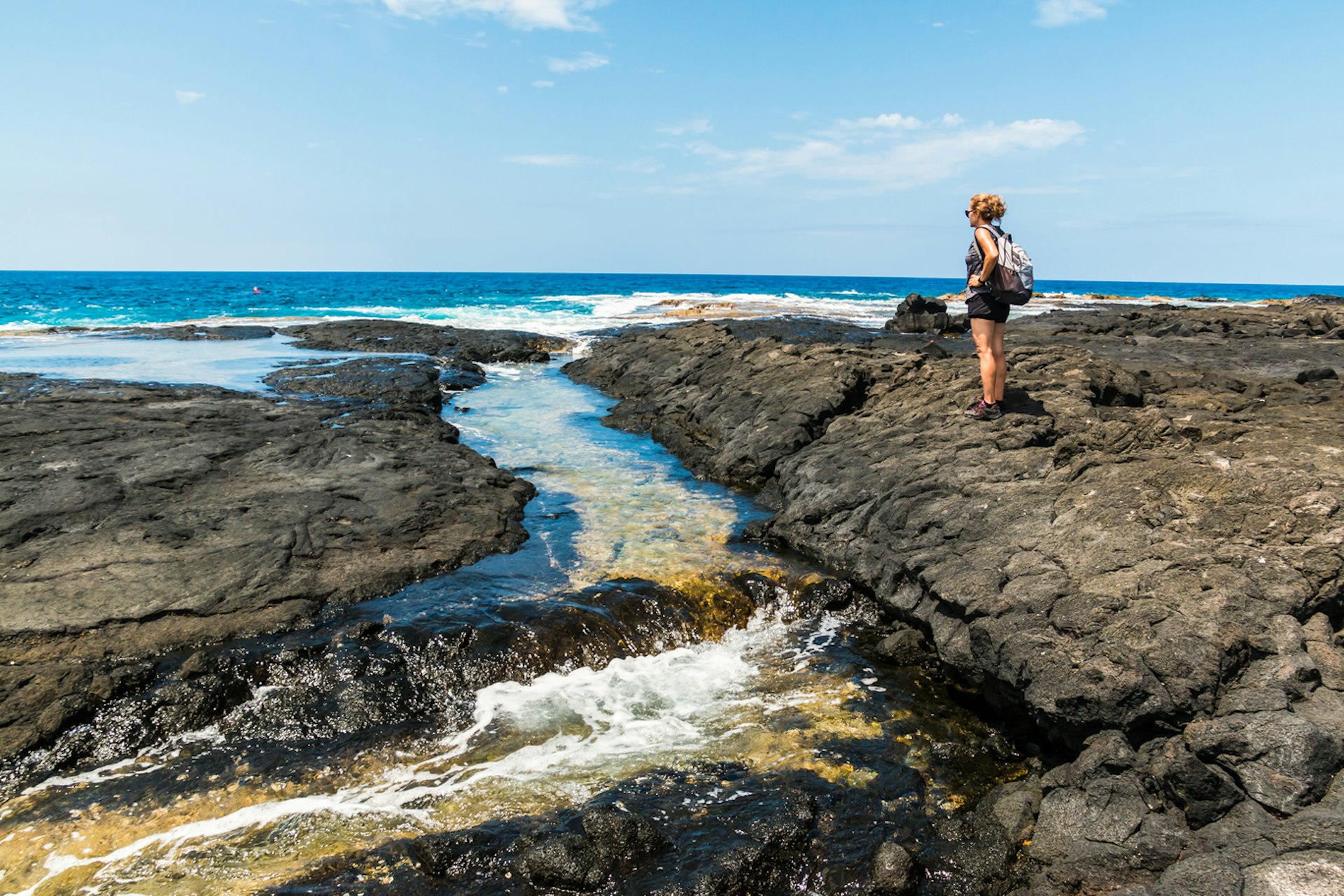 A hiker stands in lava field looking out to sea 