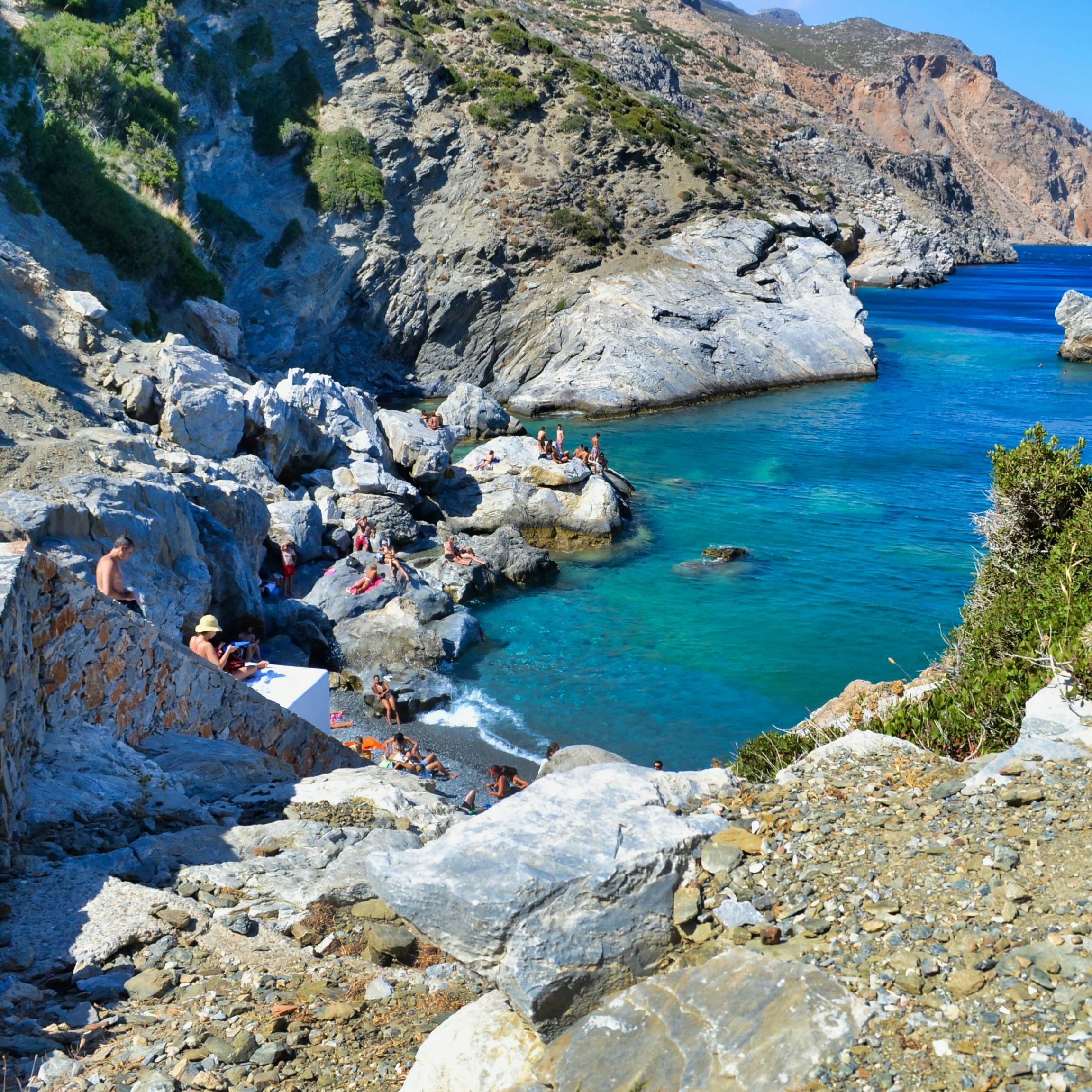 People sunbathing on the rocks in Agia Anna beach at Amorgos island of Greece.