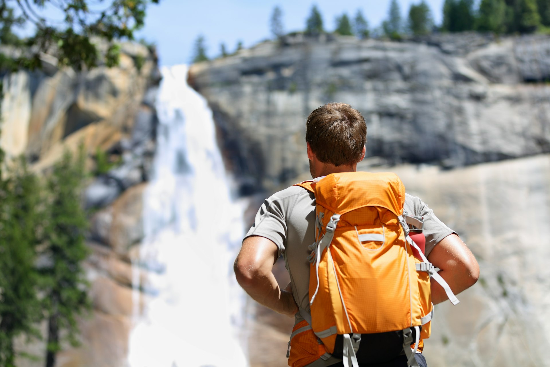 Hiker hiking with backpack looking at waterfall in Yosemite park in beautiful summer nature landscape. 