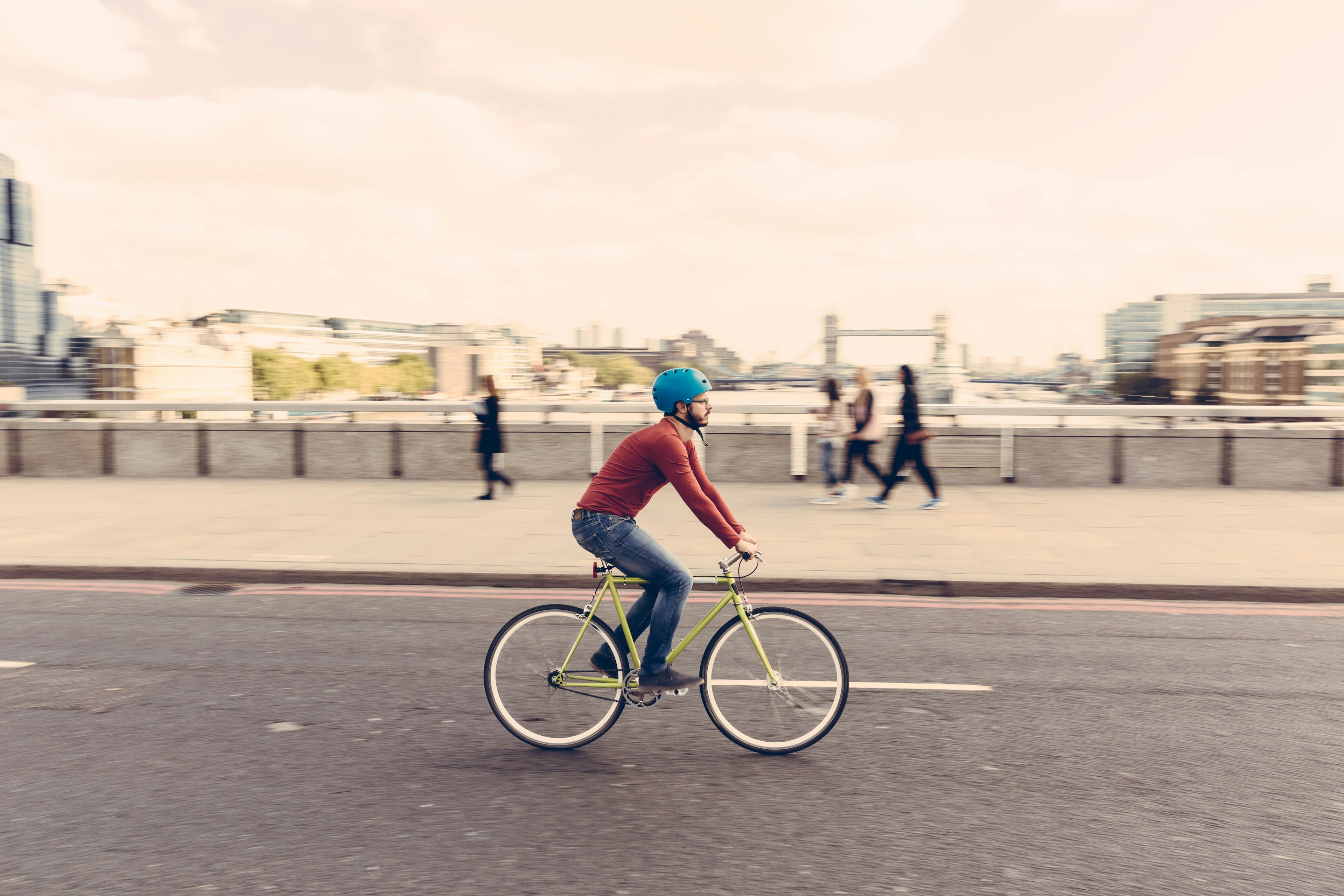 A man cycles on a bridge at dusk across the Thames with Tower Bridge in London, England, United Kingdom