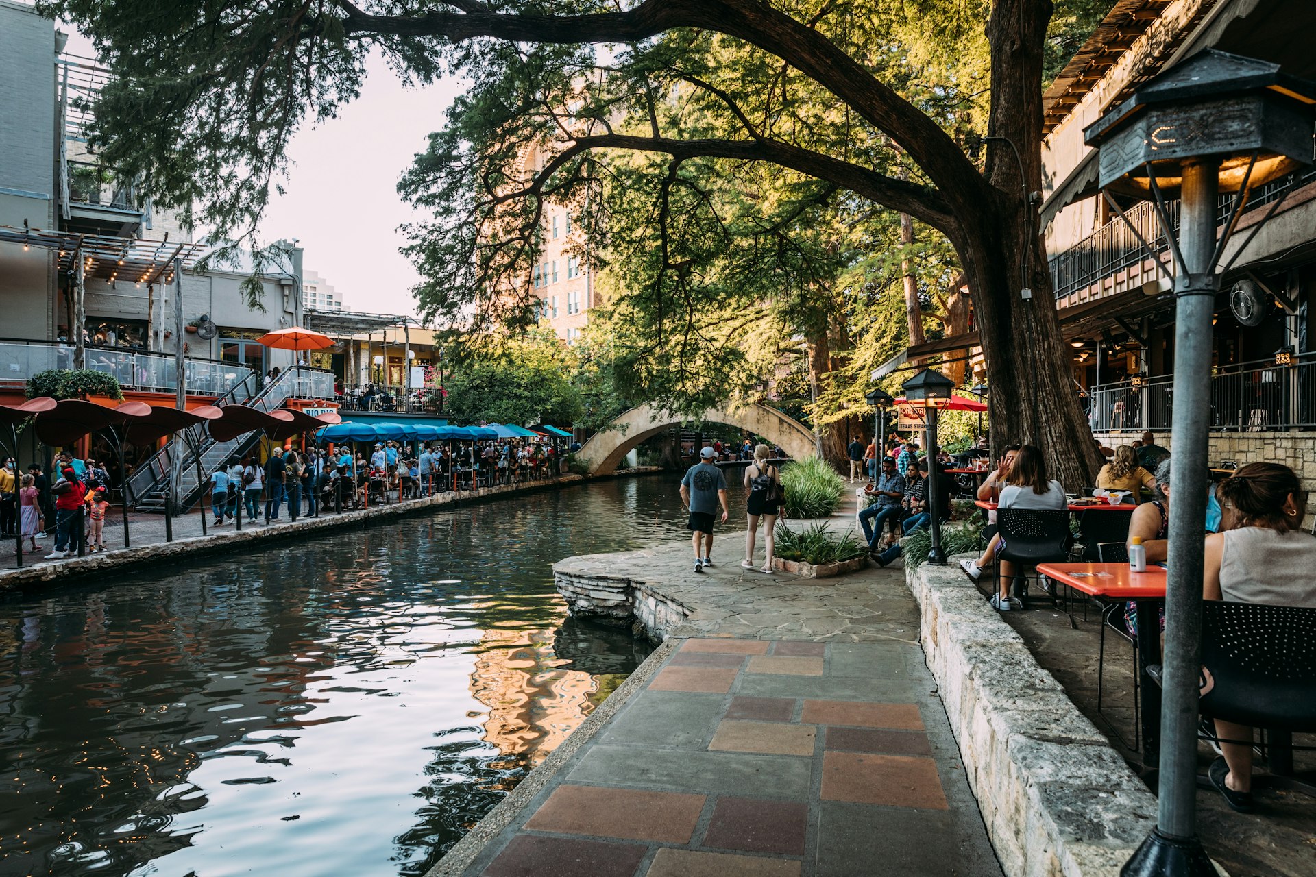 Street view of people walking and dining along the San Antonio River Walk