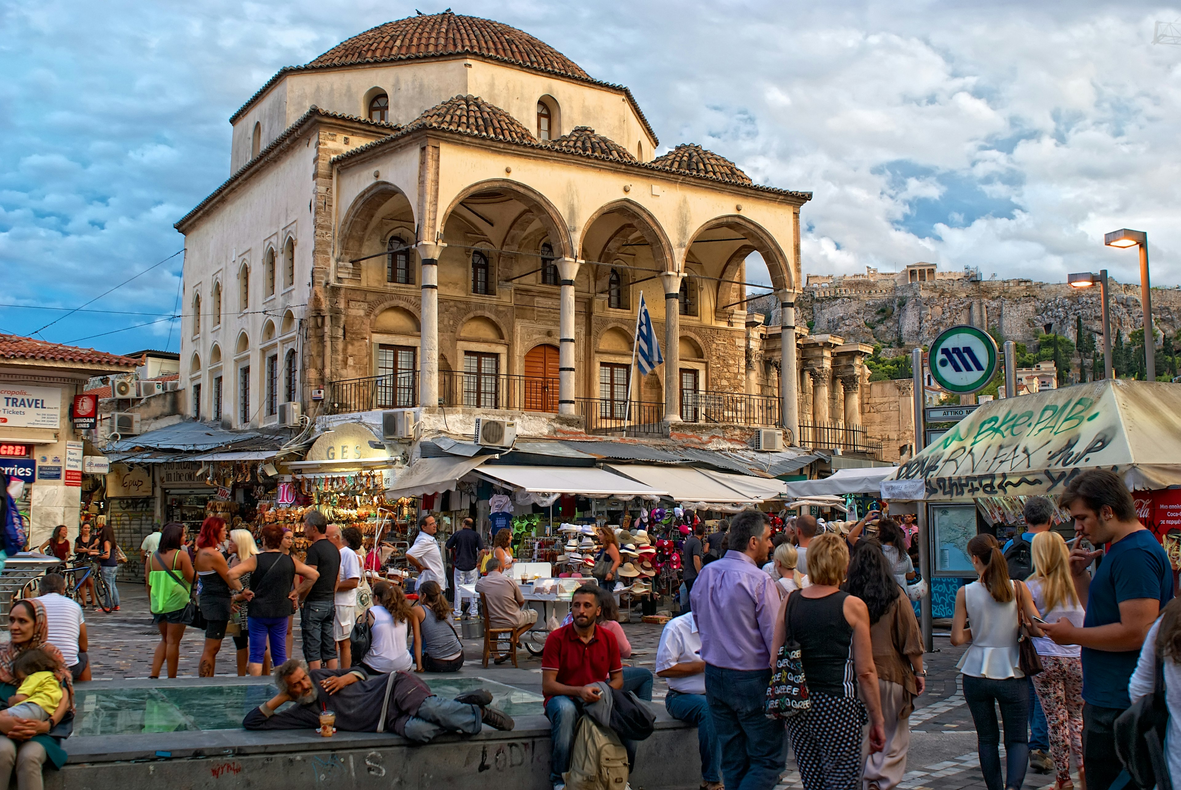 A large building, with four columns supporting its roof, is surrounded by stalls selling clothes, shoes and souvenirs