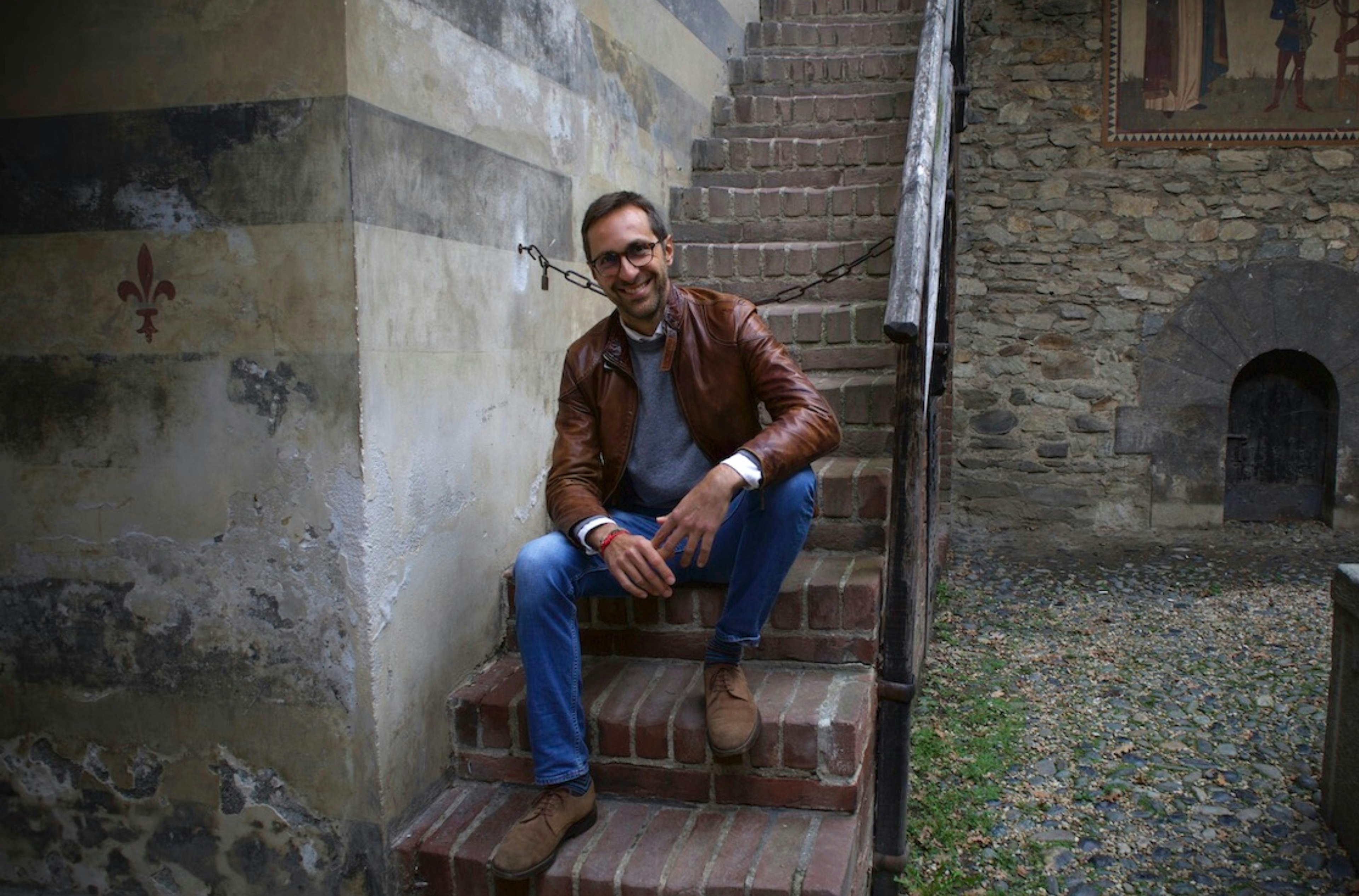 Elsewhere guide Andrea sitting on brick stairs by an old stone building