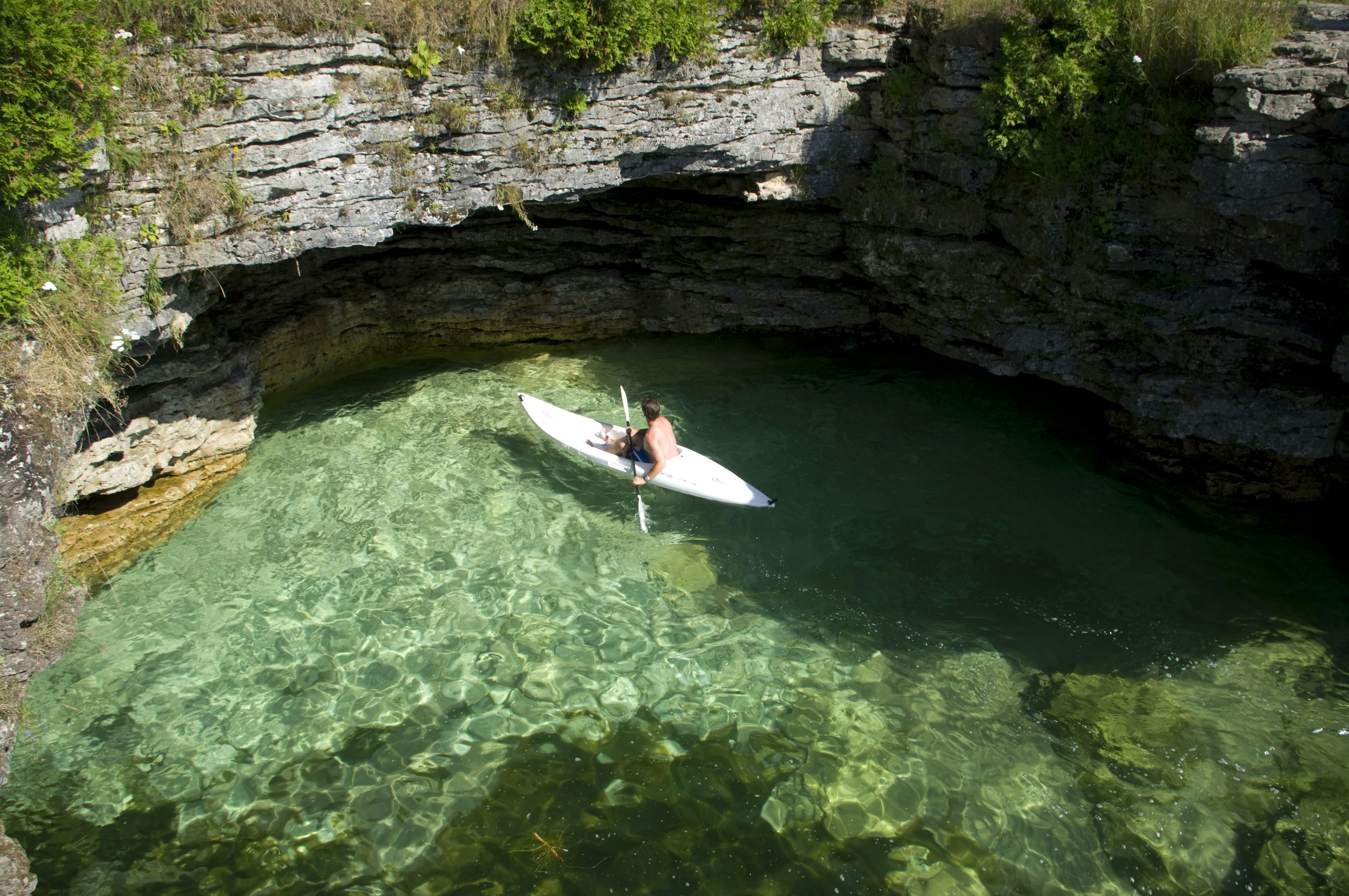 A solo kayaker paddles towards a rocky overhang