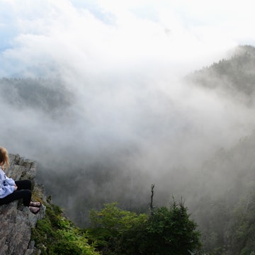A teenage girl sits and watches drifting clouds at the summit of Mount LeConte in the Great Smoky Mountains National Park.