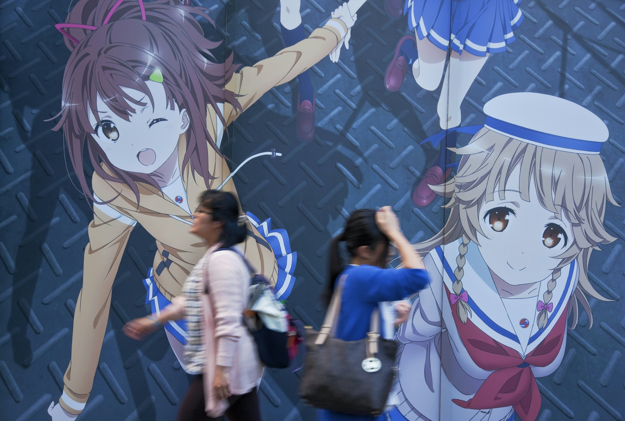 Two young women walking in opposite directions past a wall-sized anime mural along Chuo-dori (Central Avenue) in the Akihabara district