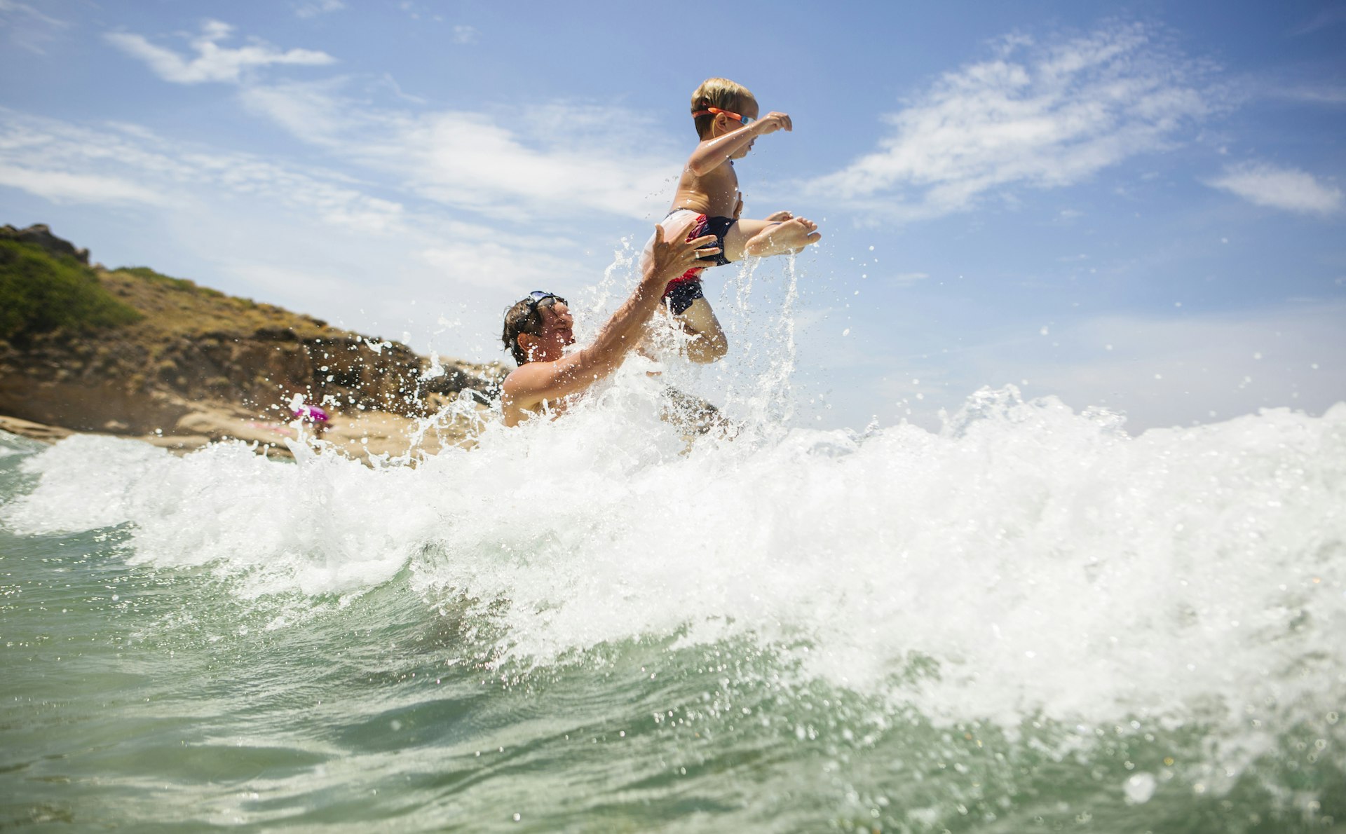 A man lifts a small child over the waves at the beach in Calvi, Corsica