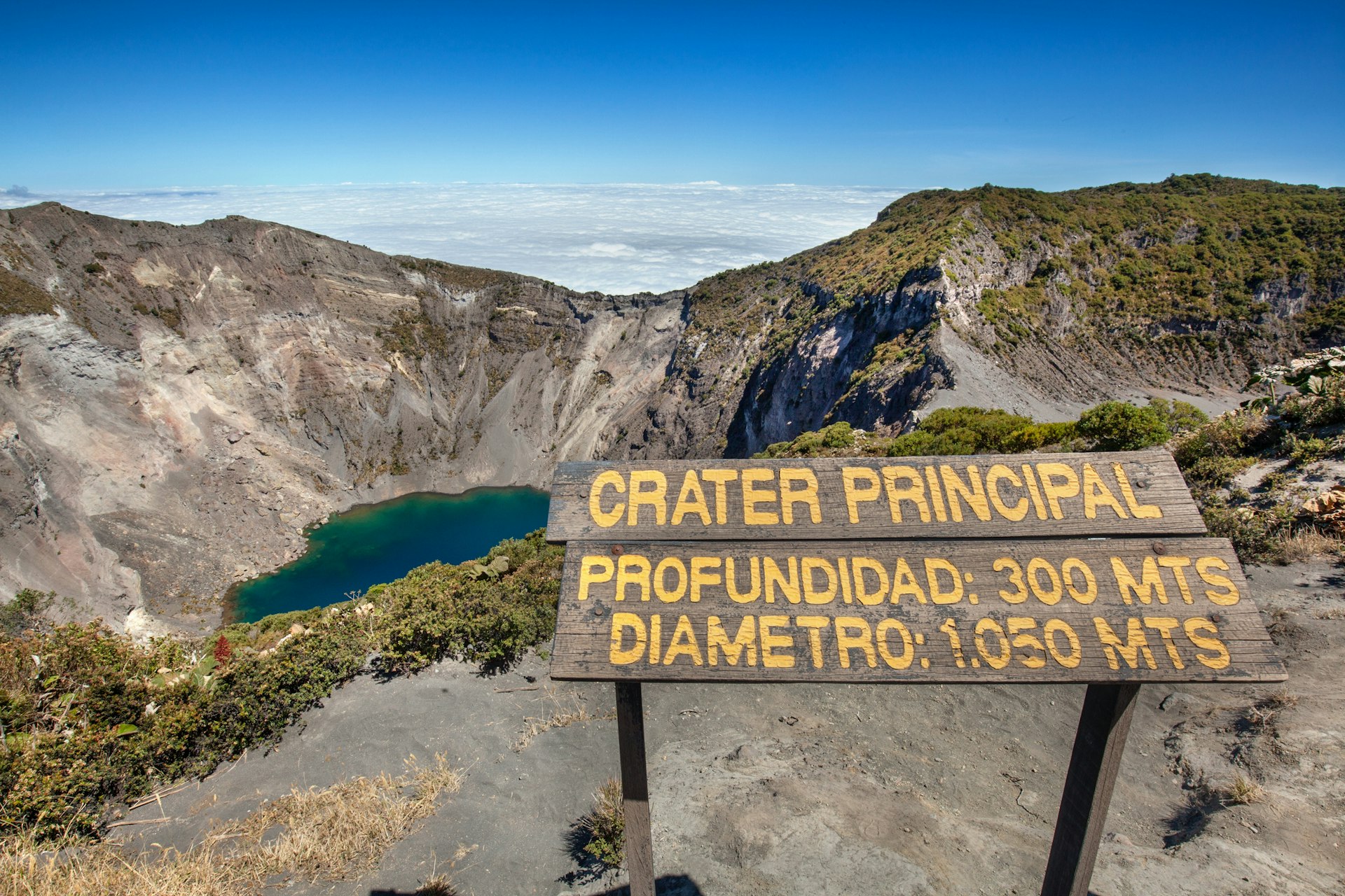 A sign at a volcanic crater filled with blue-green water that says "Crater Principal"