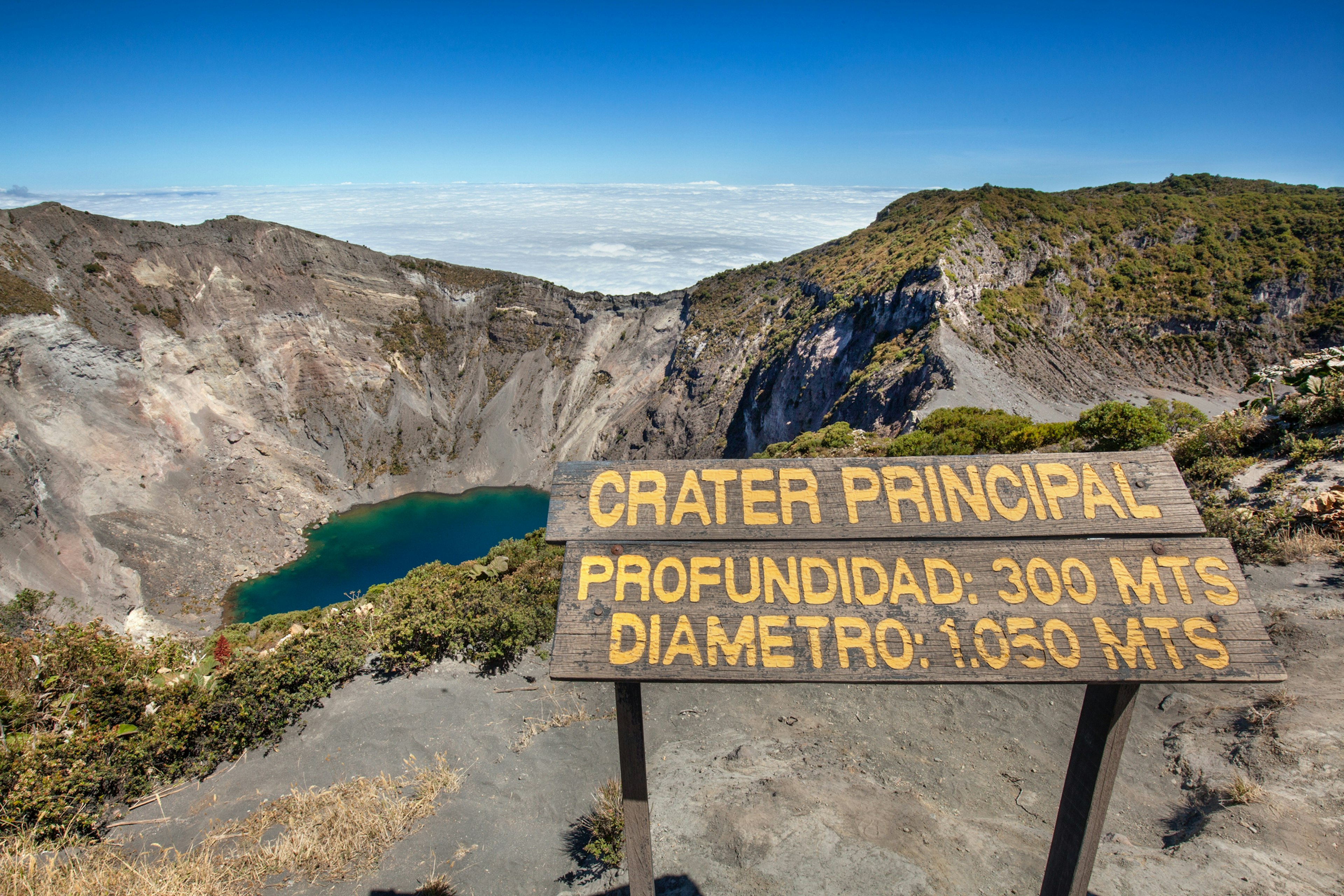 A sign at a volcanic crater filled with blue-green water that says