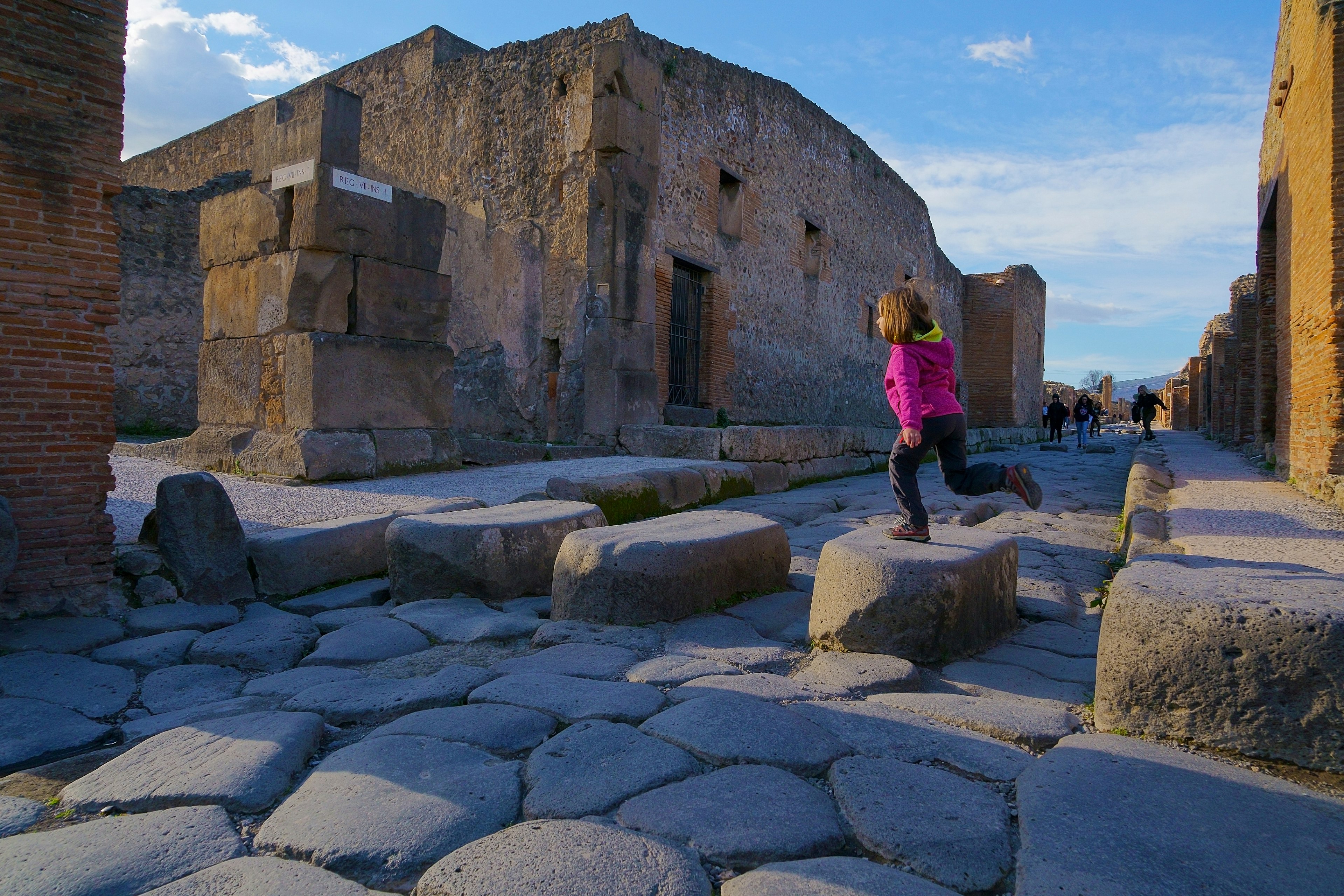 A girl jumps on large stones on a former street of ancient Pompeii, Catania, Italy