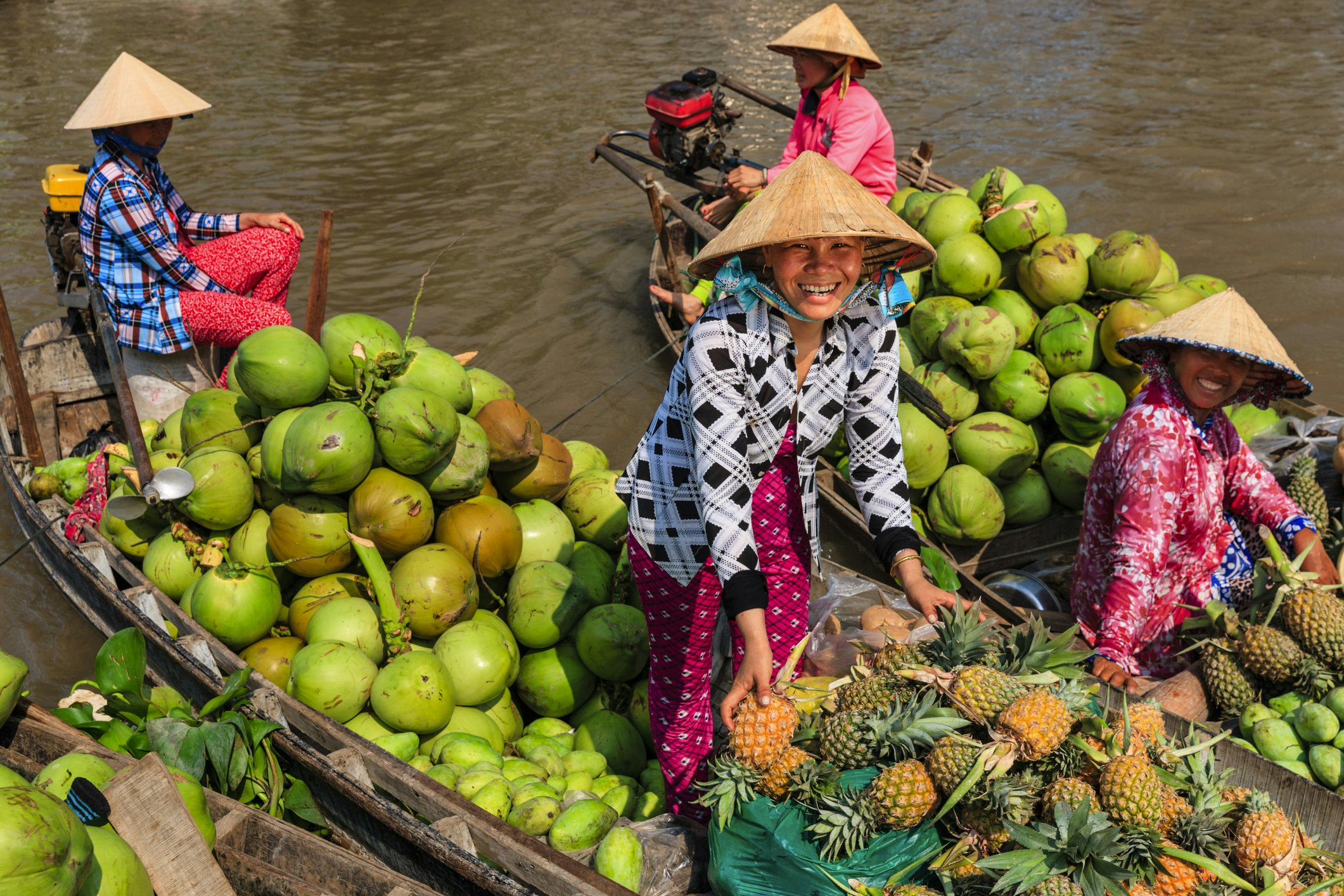 A woman in a pointed straw hat sells fruits from a boat at a floating market