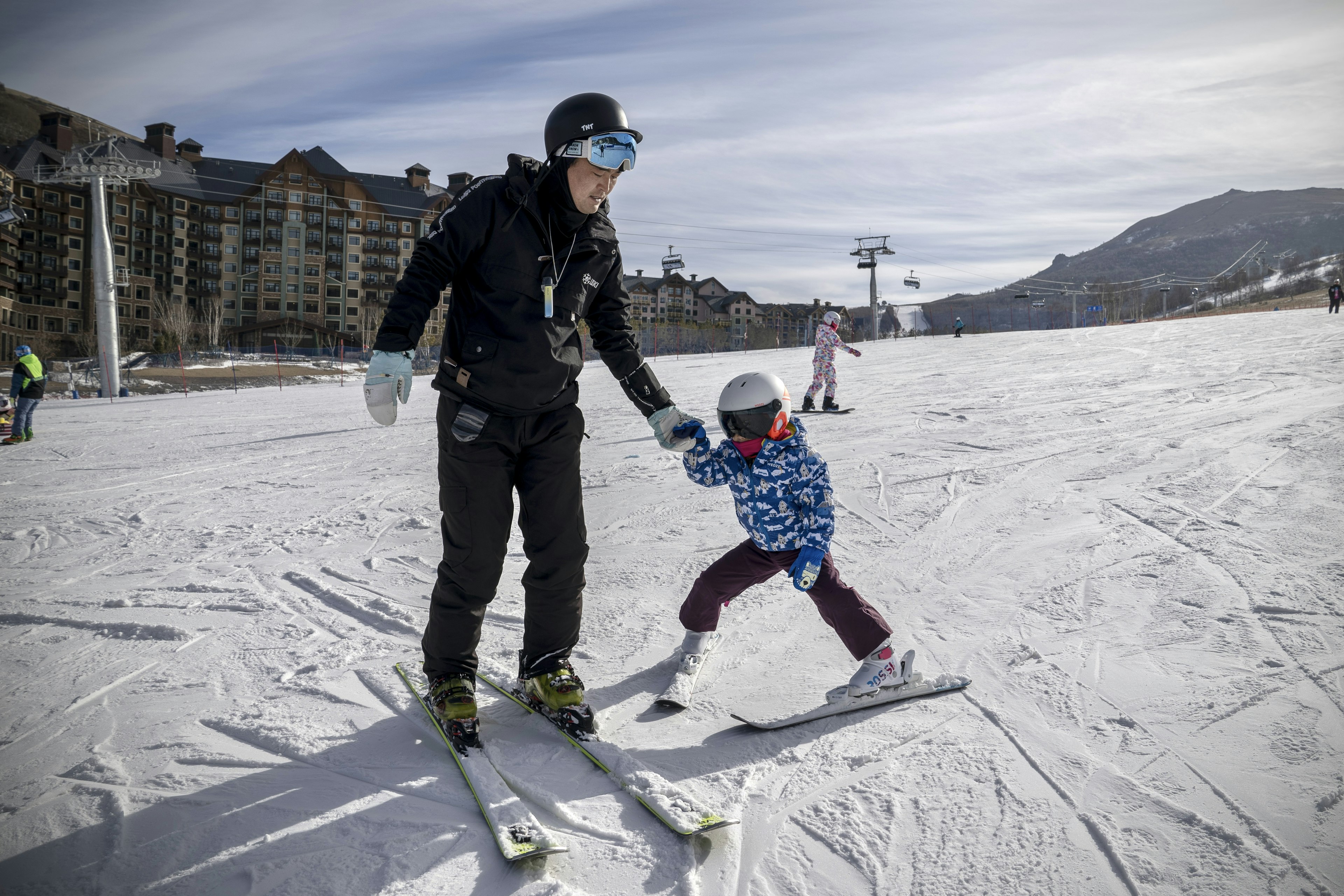 A father and child on skis at the bottom of a slope at Thaiwoo Ski Resort, Chongli, Zhangjiakou, Hebei, China