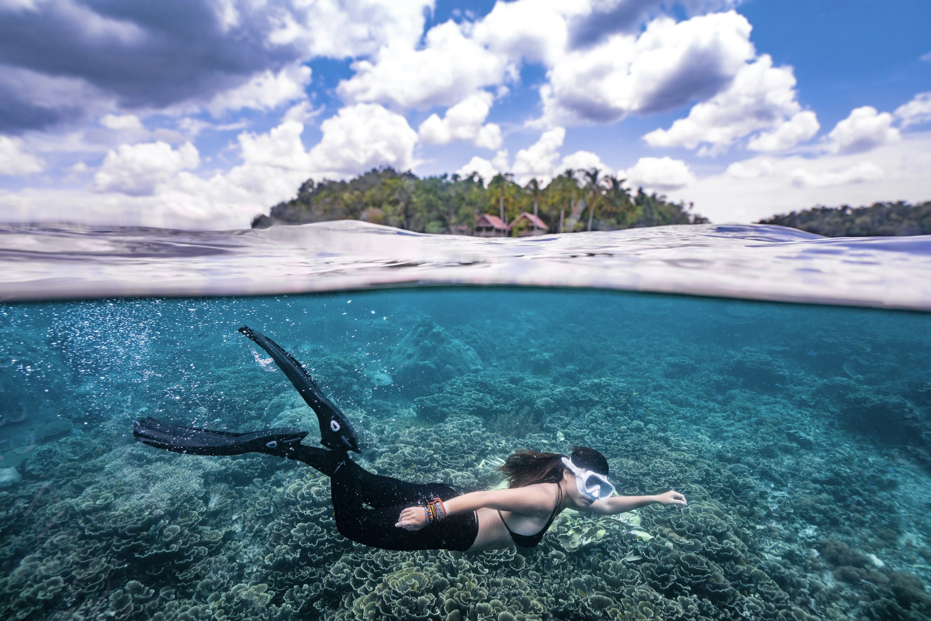 Split shot of a free diver swimming beneath the ocean at Raja Ampat with small island on the surface
