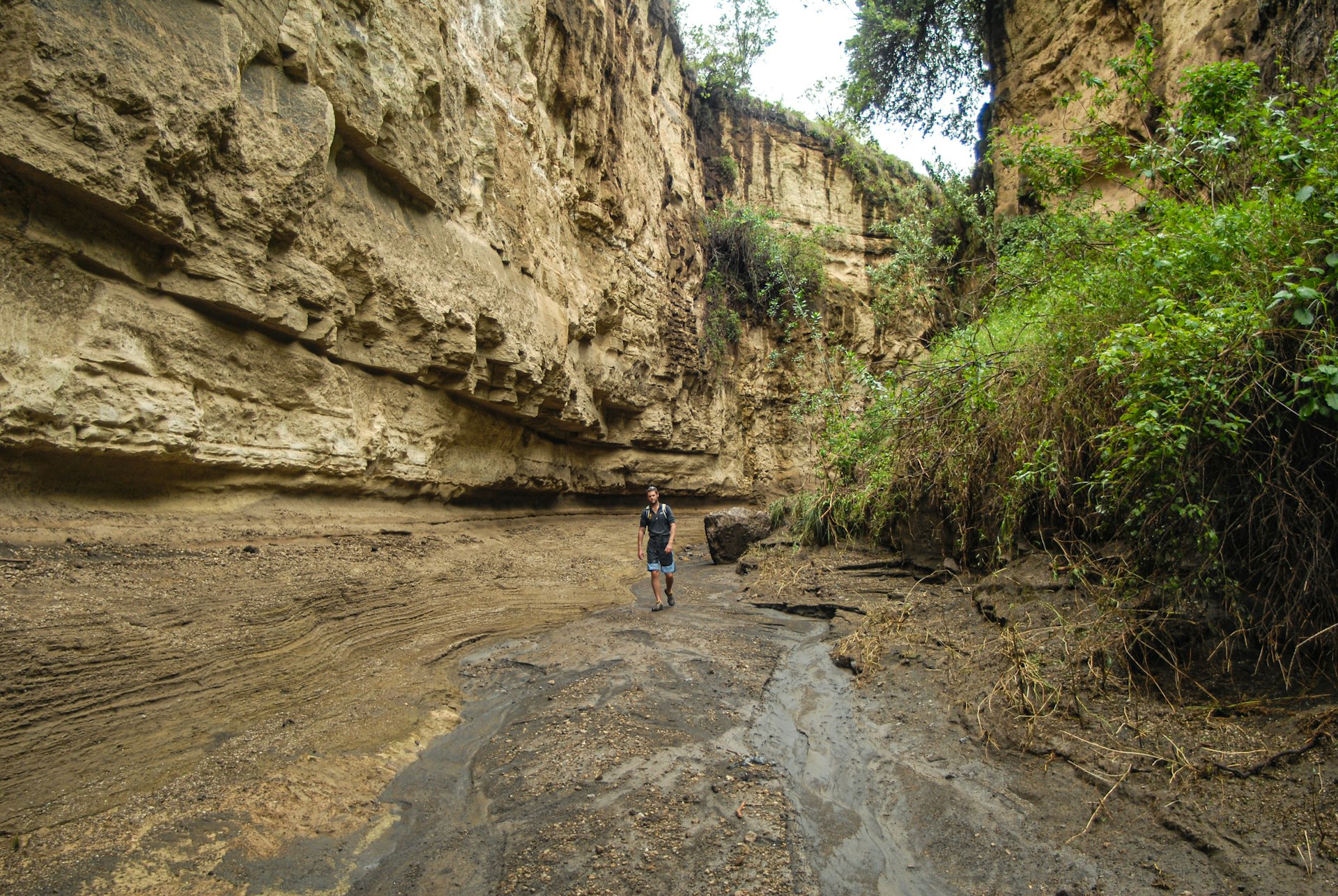 A man walks through a narrow pathway between sheer walls of volcanic rock in a national park