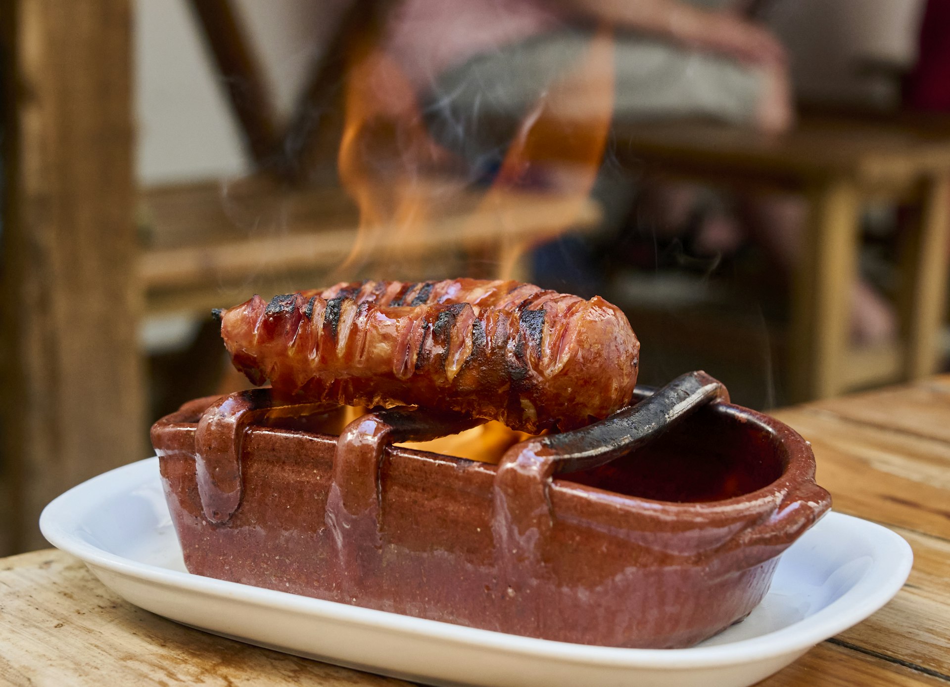 Un chouriço asado de cerdo negro (salchicha a la parrilla) se cocina a la llama sobre alcohol en una parrilla de terracota en Casa do Alentejo, Lisboa, Portugal, Europa